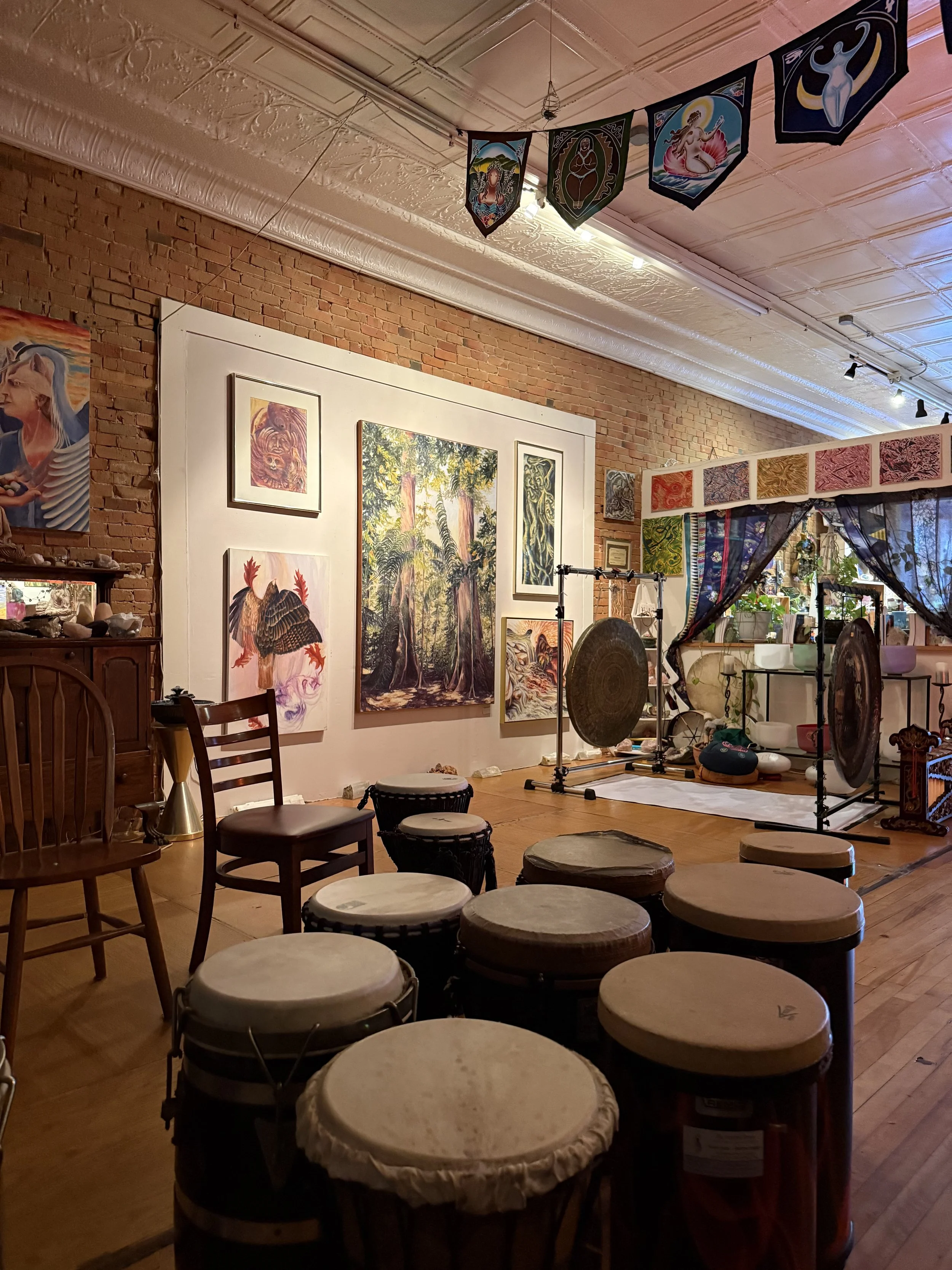 Indoor art gallery with various paintings, drums, and decorations on brick walls and ceiling.