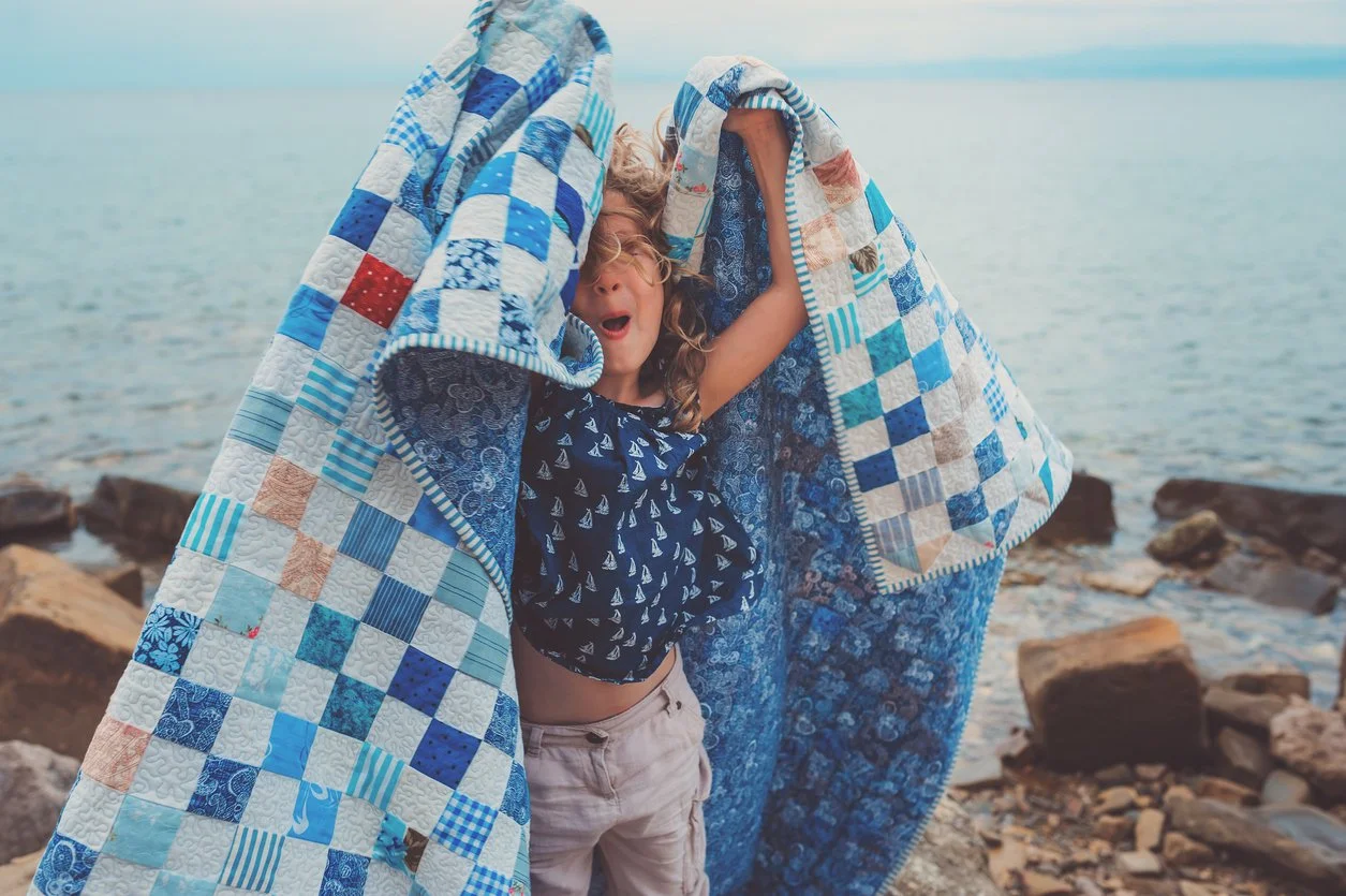 girl with blue and white quilt on rocky shore