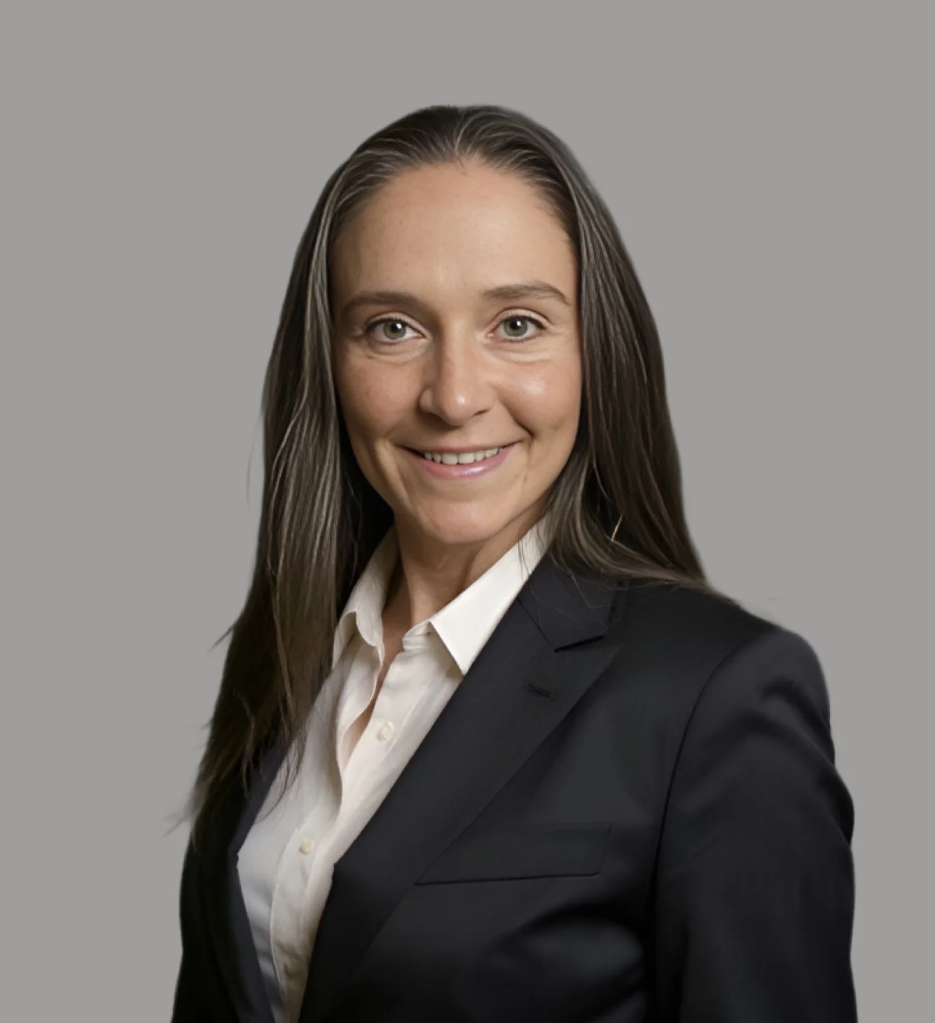 A professional woman with long brown hair wearing a black blazer and white shirt, smiling against a gray background.