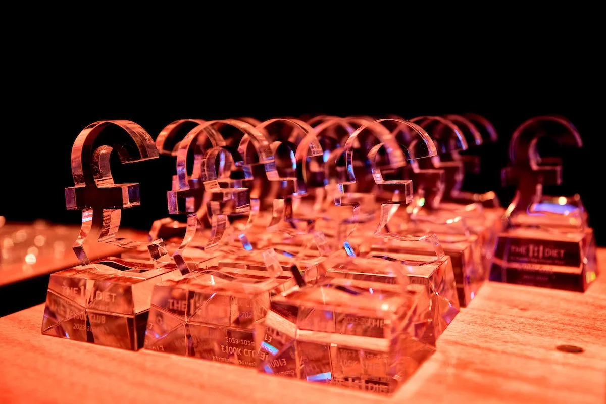 Several crystal trophies with a Euro symbol on top, arranged on a wooden surface under red and blue lighting.