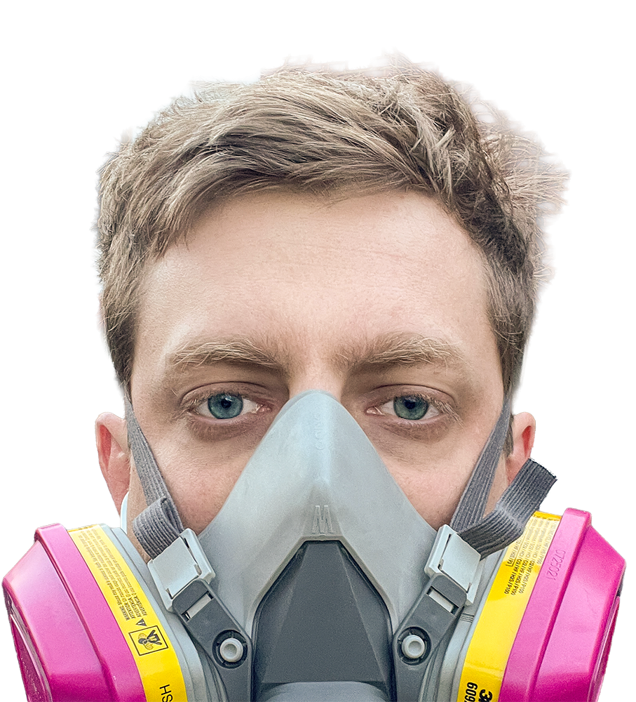 Man wearing a gray respirator mask with pink filters and yellow warning labels.