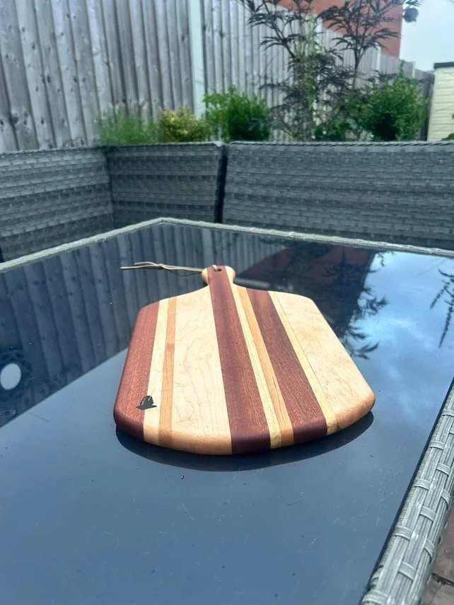 A wooden cutting board with a striped pattern in shades of brown and tan, placed on a glass outdoor table.
