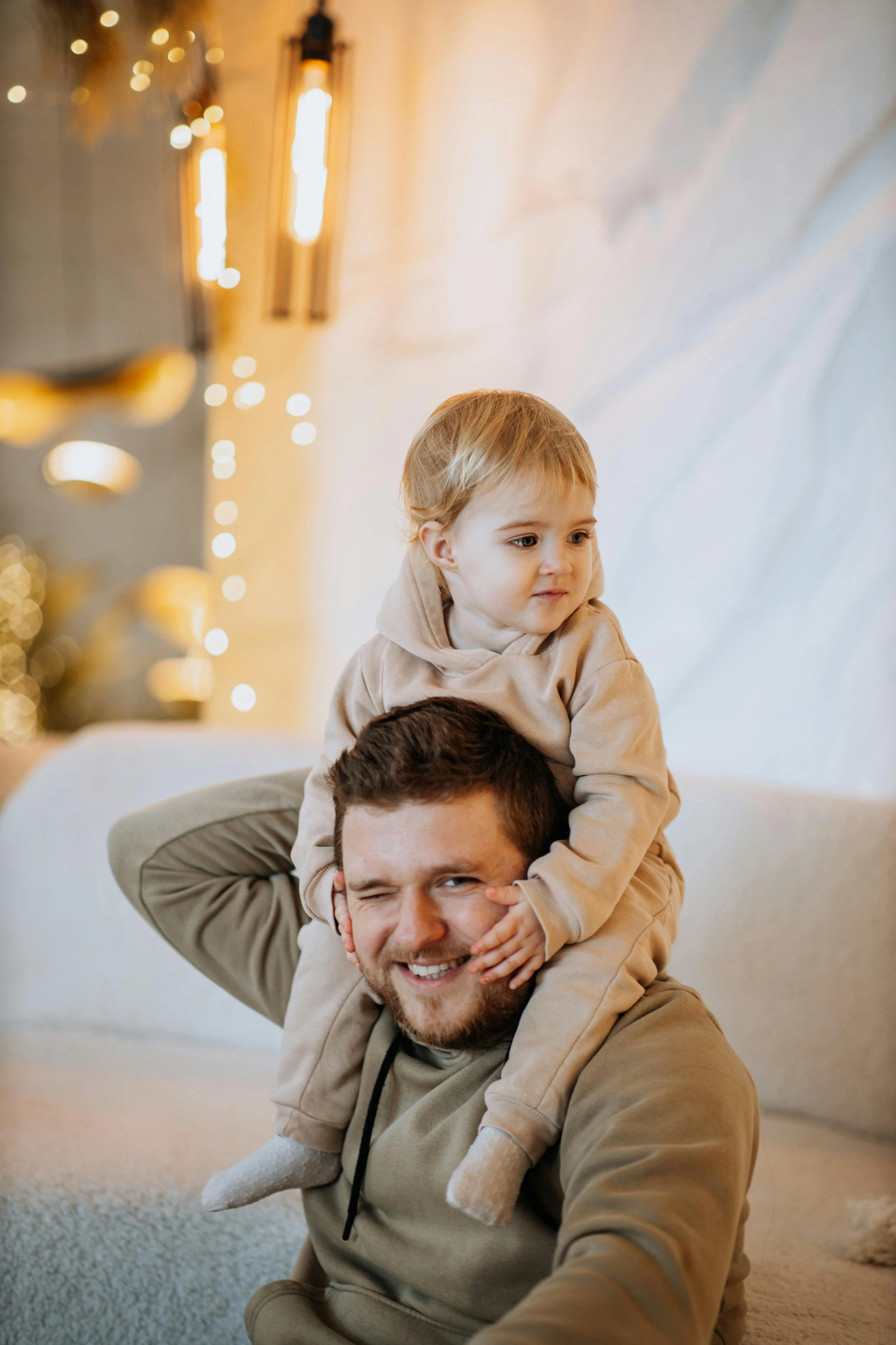 A man giving a piggyback ride to a young boy in a cozy, warmly lit living room decorated for the holidays.