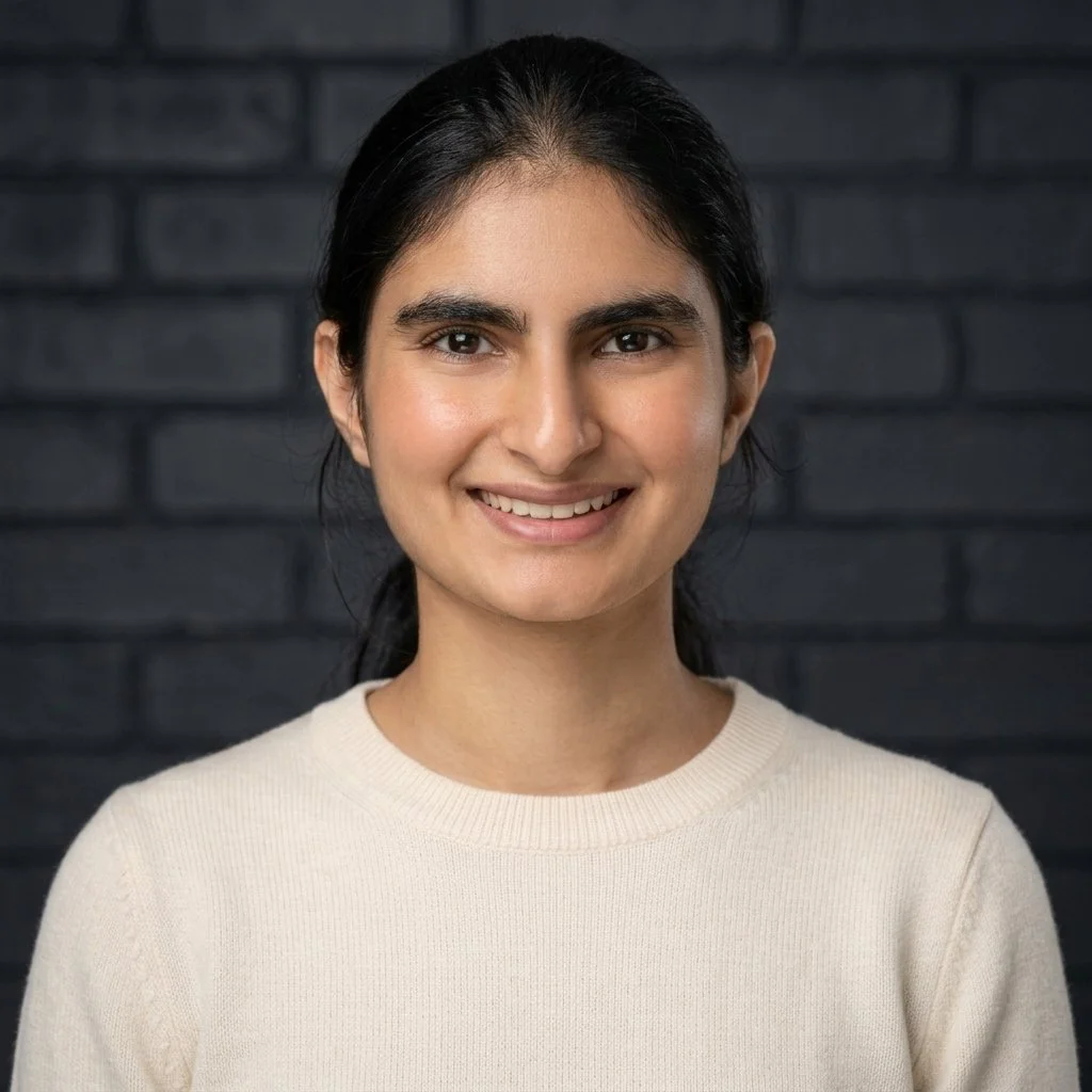 Portrait of a smiling woman with dark hair in front of a dark gray brick wall.