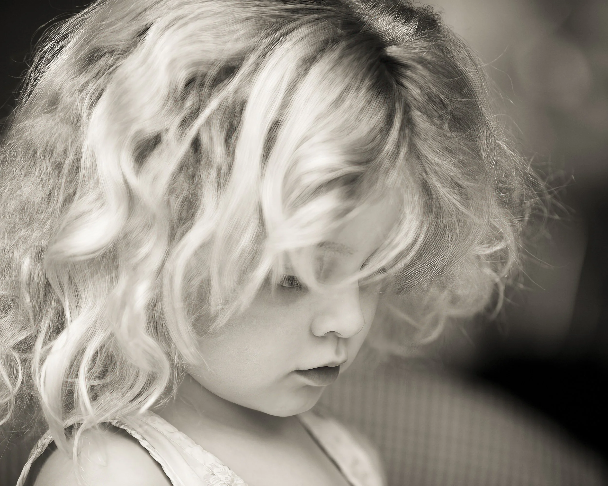 A young girl with curly blonde hair looking downward, in a black and white portrait.