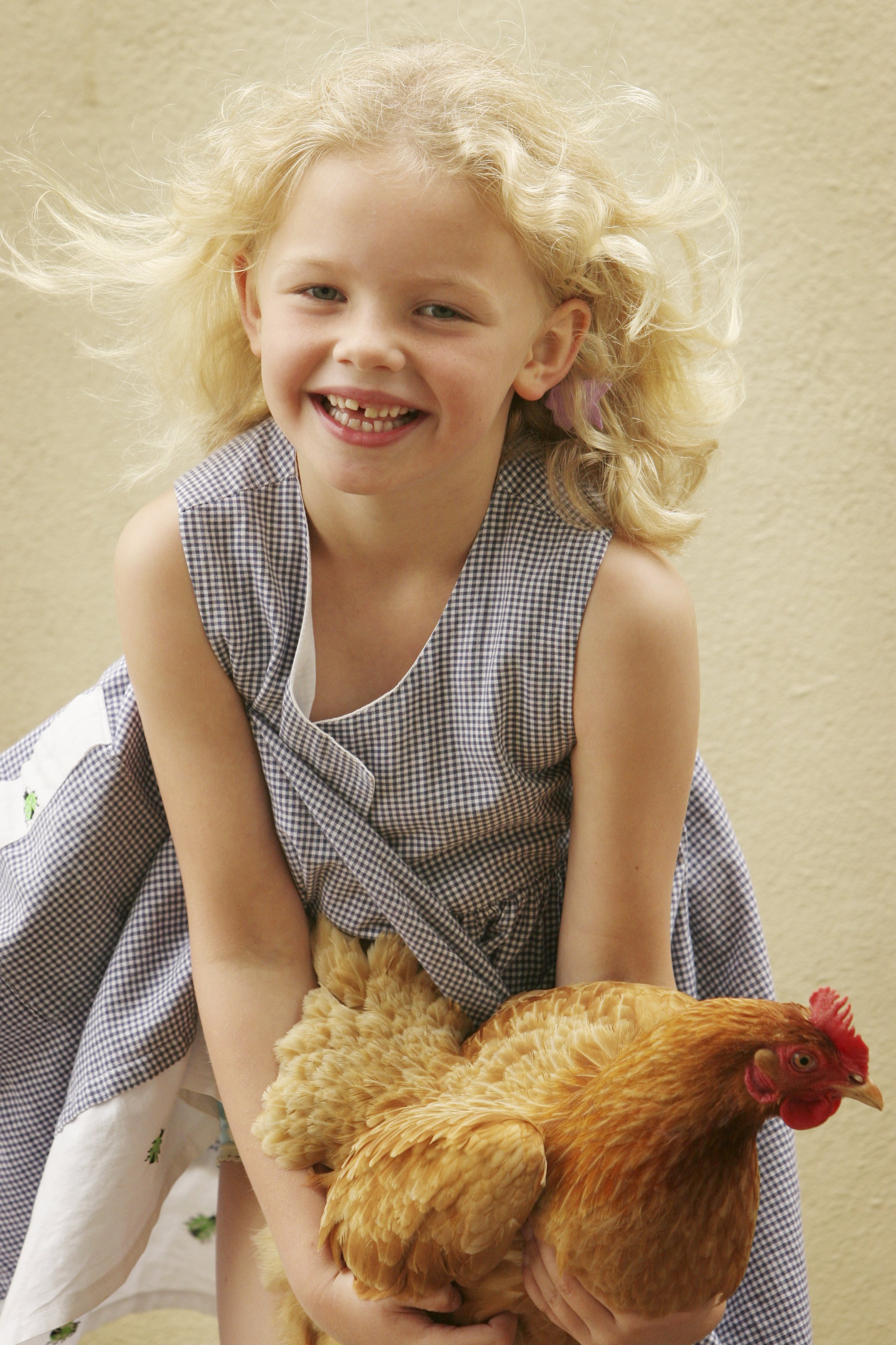 A young girl with curly blonde hair smiling and holding a chicken.