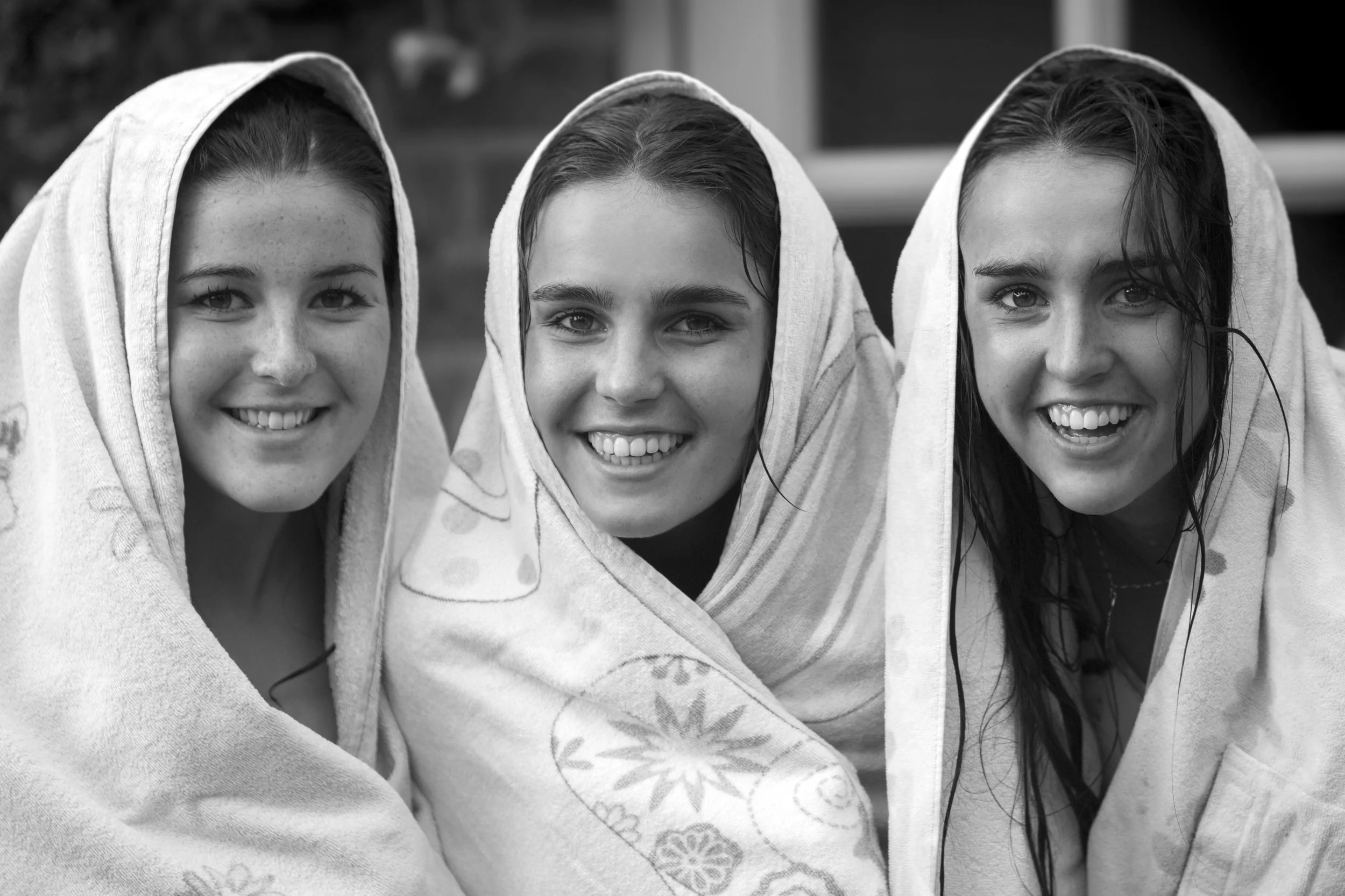 Three young girls wrapped in towels, smiling, outdoors in black and white.