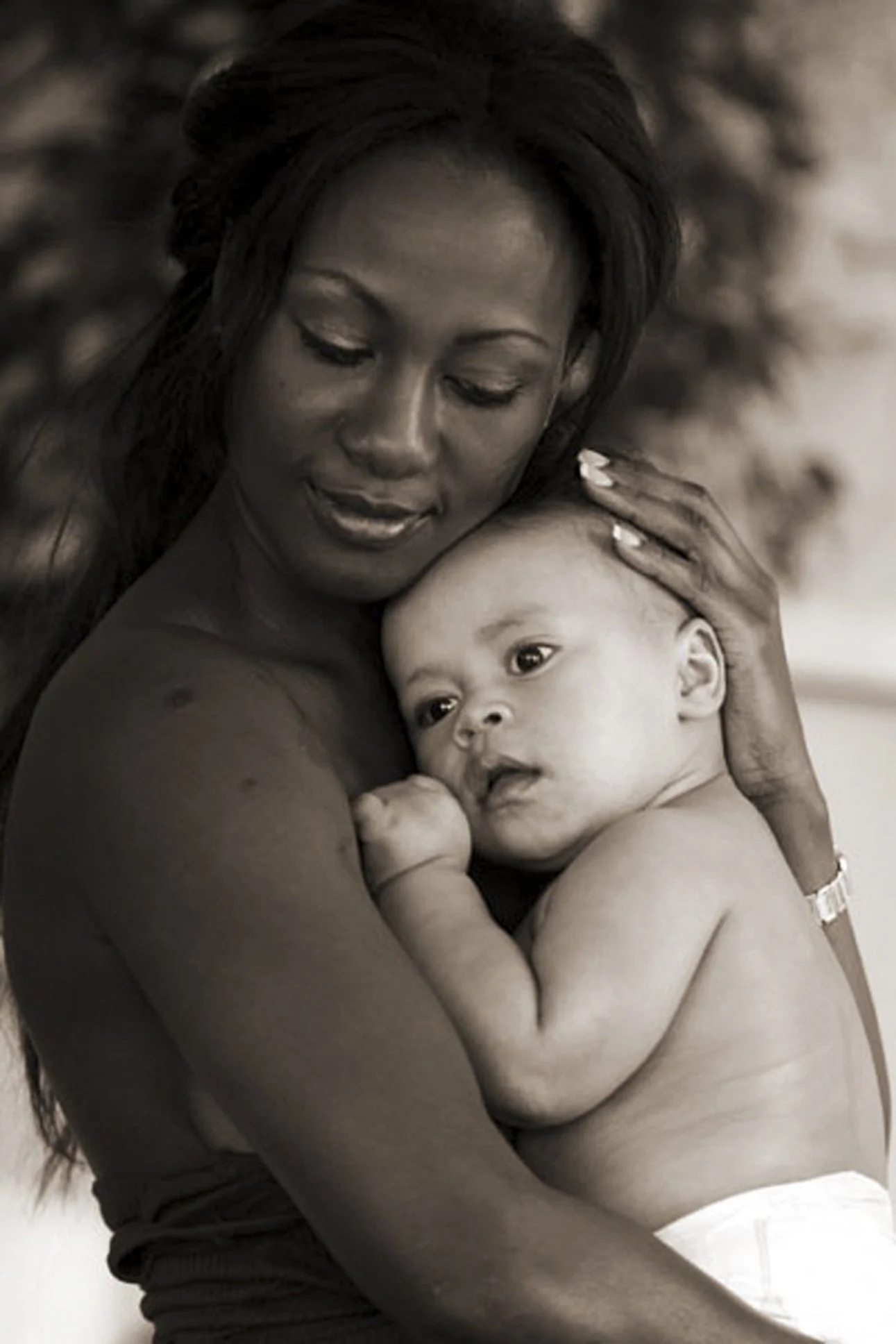 A woman lovingly holding a baby close to her chest, both with tender expressions, in a black and white photograph.
