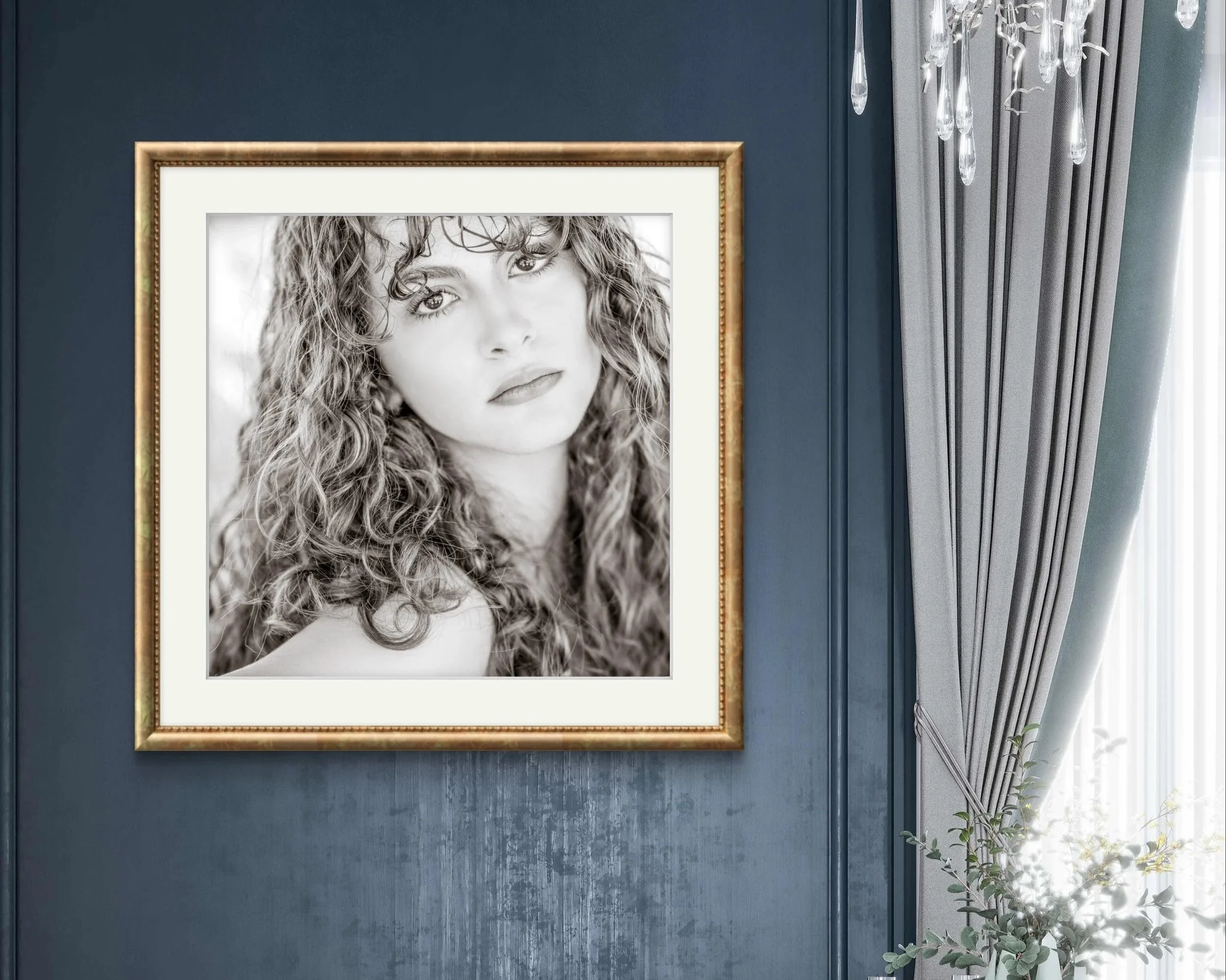 Black and white portrait of a woman with curly hair, framed and hanging on a blue wall in a room with curtains and a chandelier.