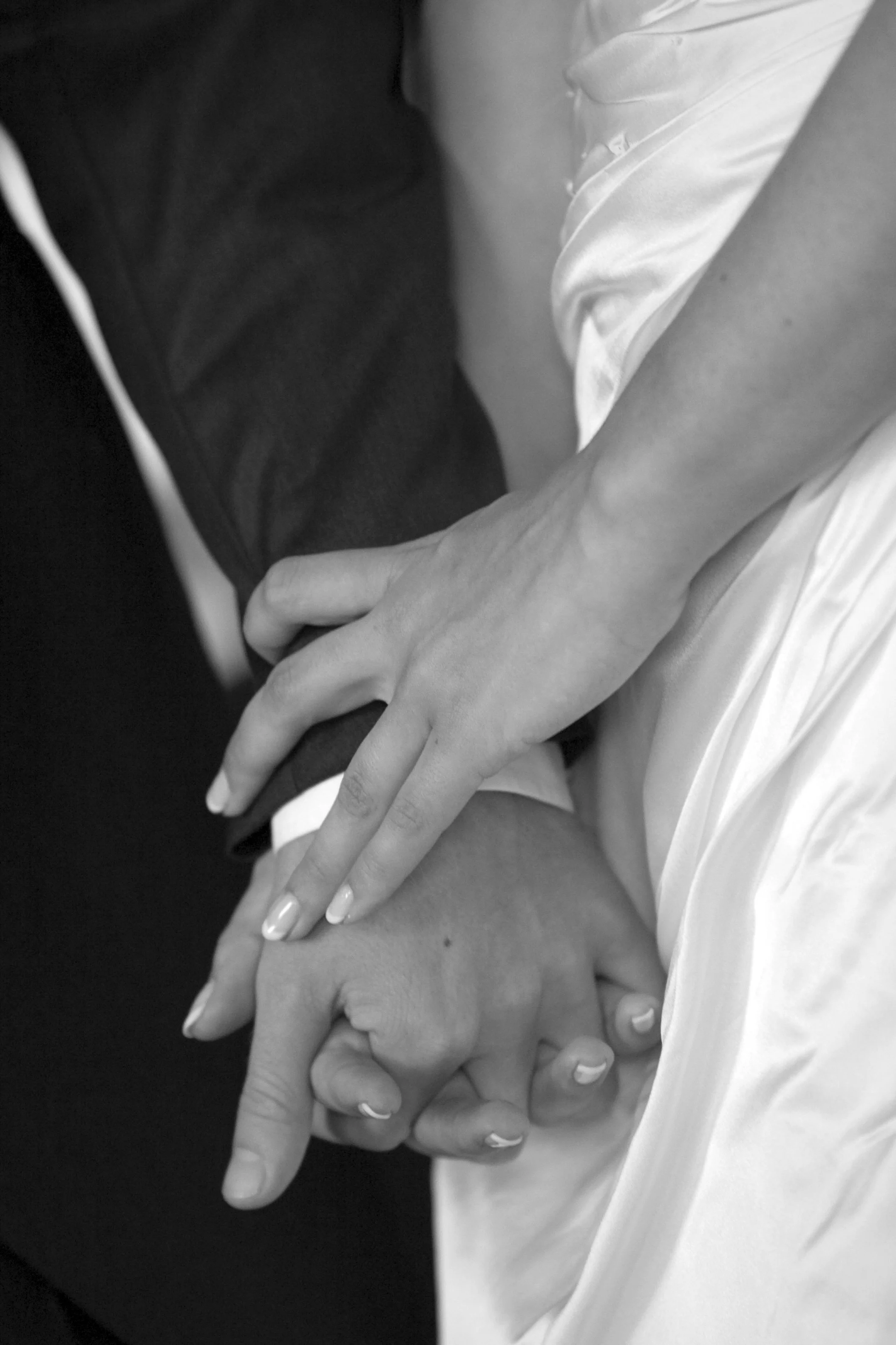 Close-up of a couple holding hands, one with a wedding ring, in black and white.