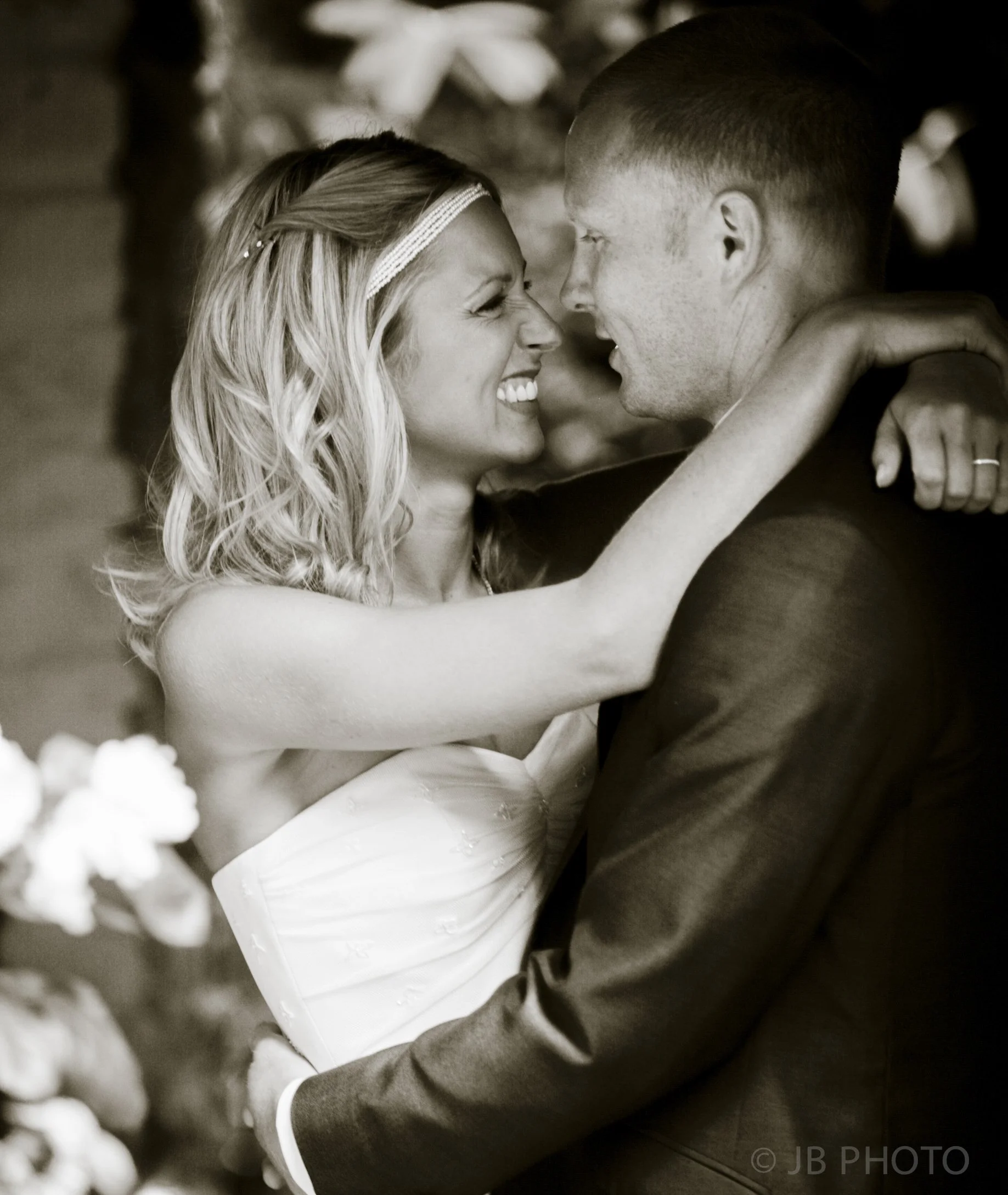A black-and-white photo of a bride and groom smiling and embracing each other during their wedding.