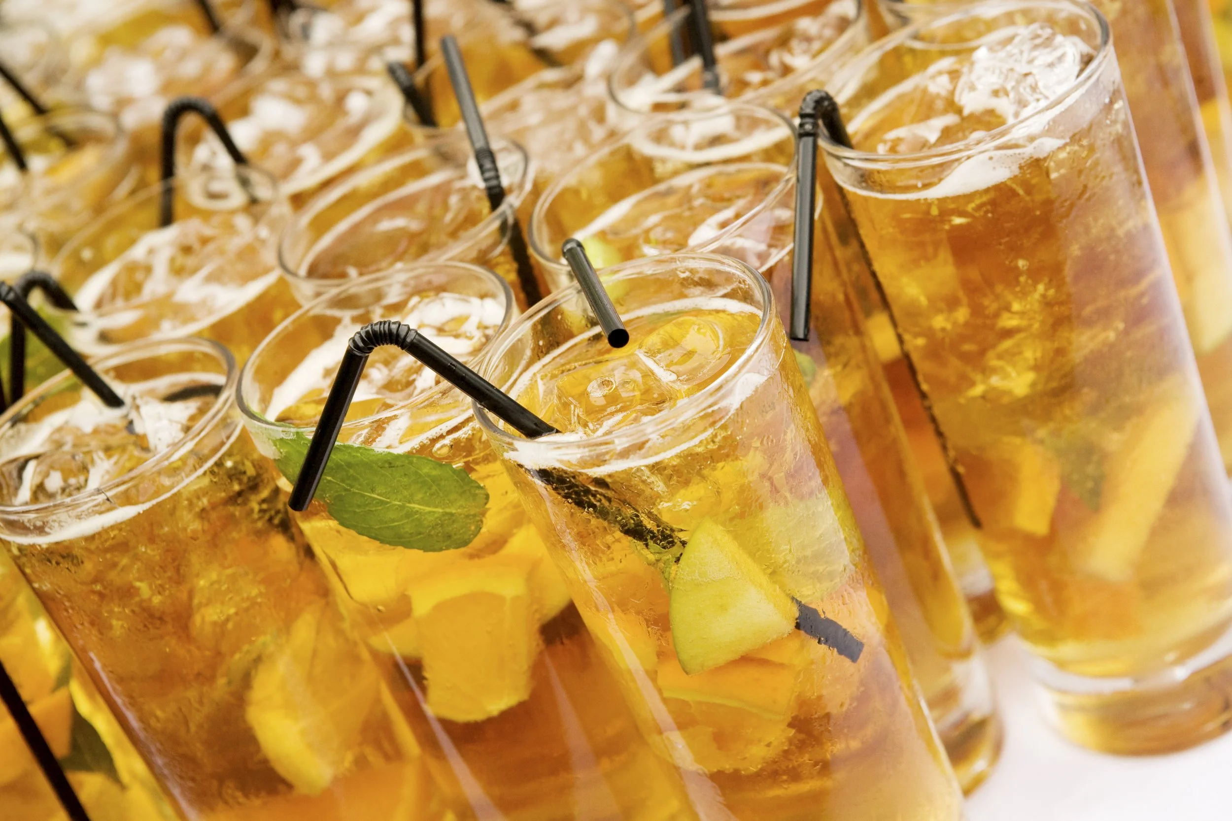 Multiple glasses of iced lemonade with lemon slices, mint leaves, and black straws, arranged in a display.