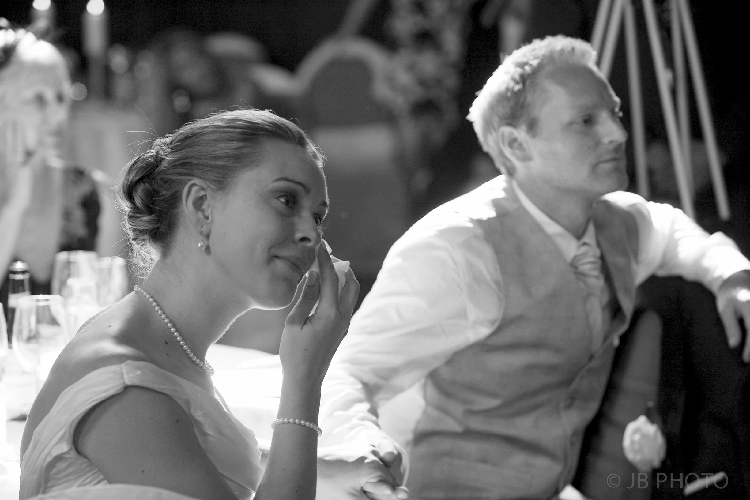 A woman and a man sitting at a formal event with the woman touching her face, both appearing to be emotional.