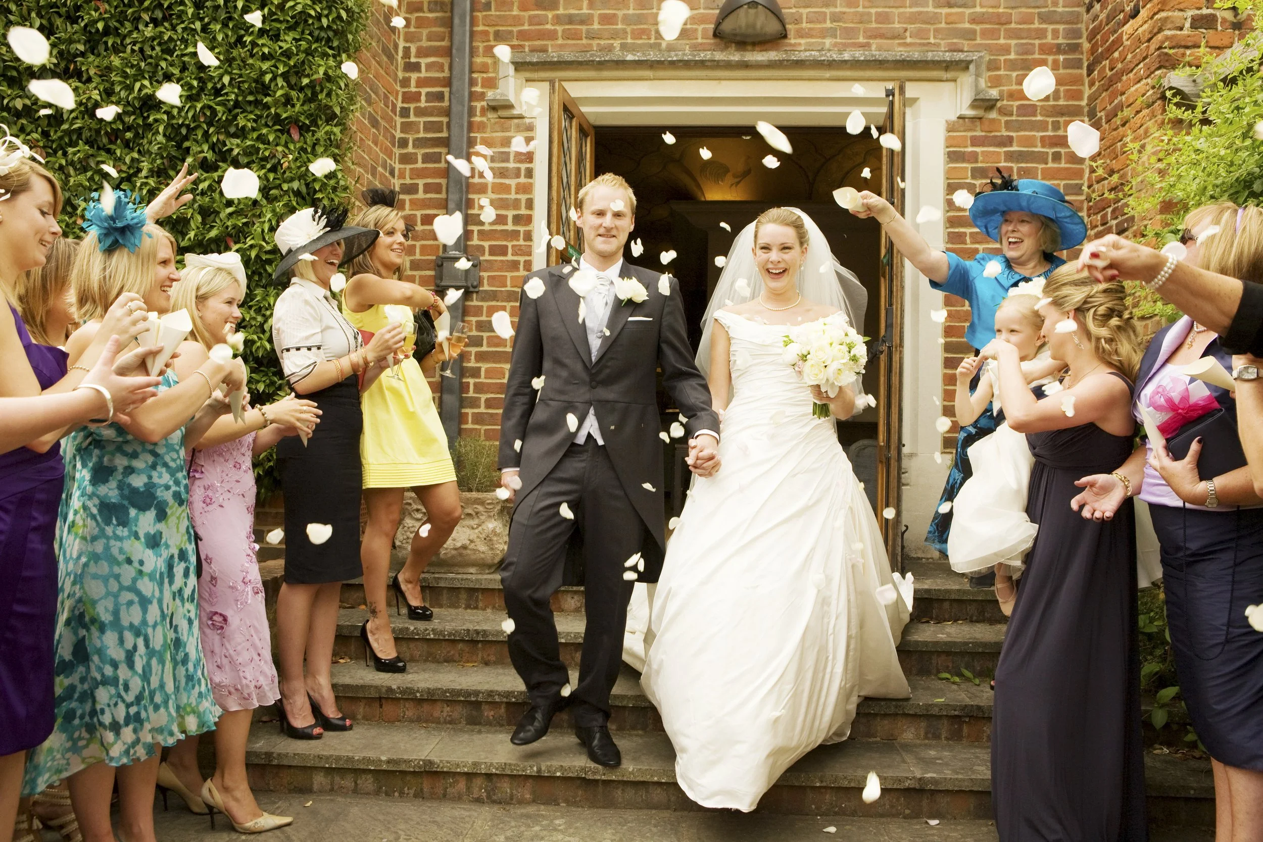 A newlywed couple walking down steps after their wedding ceremony, surrounded by friends and family throwing flower petals.