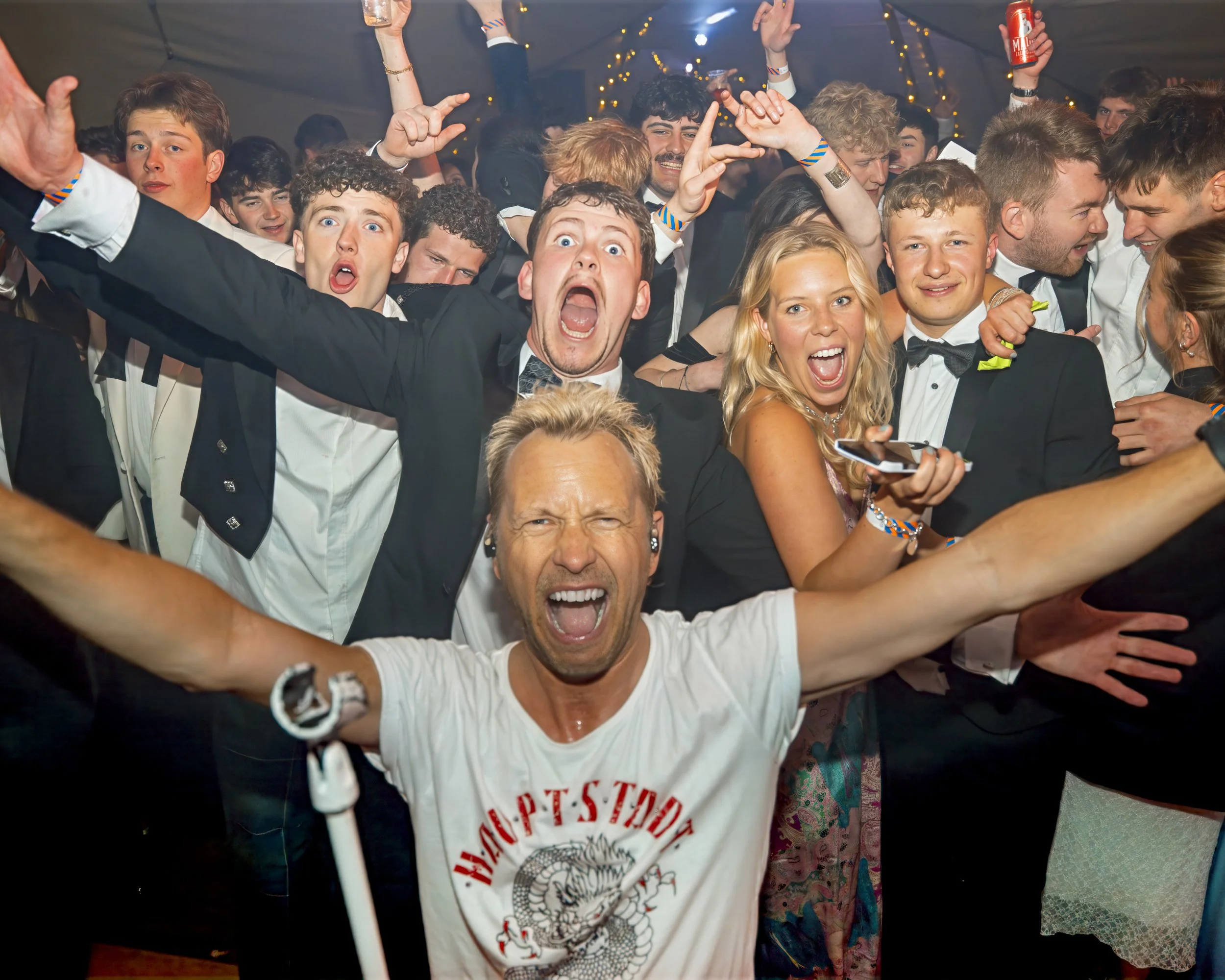 Group of young adults dressed in formal attire, celebrating at a party or dance, showing excitement and happiness.