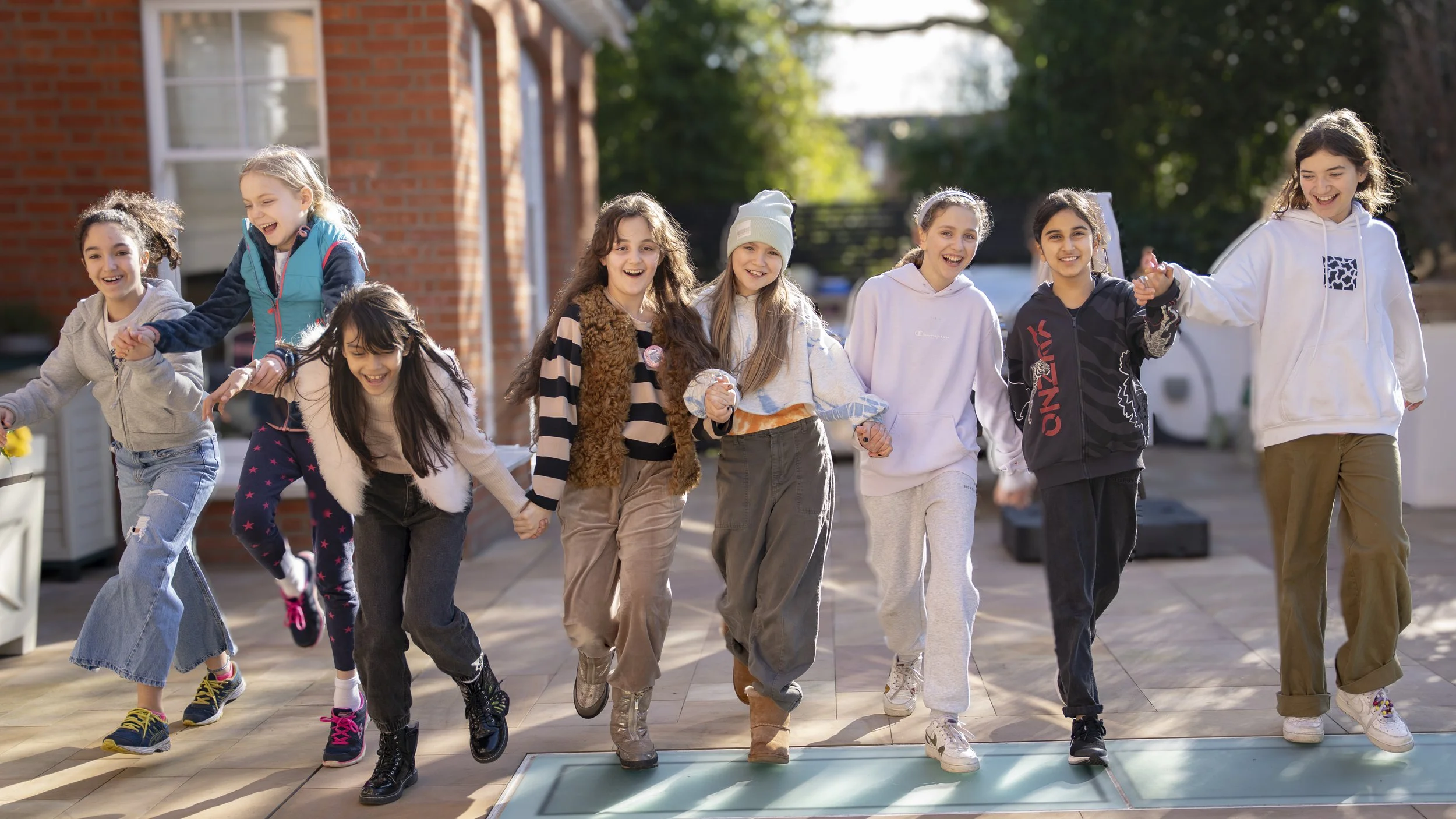 Group of children holding hands and running on an outdoor patio during daytime.