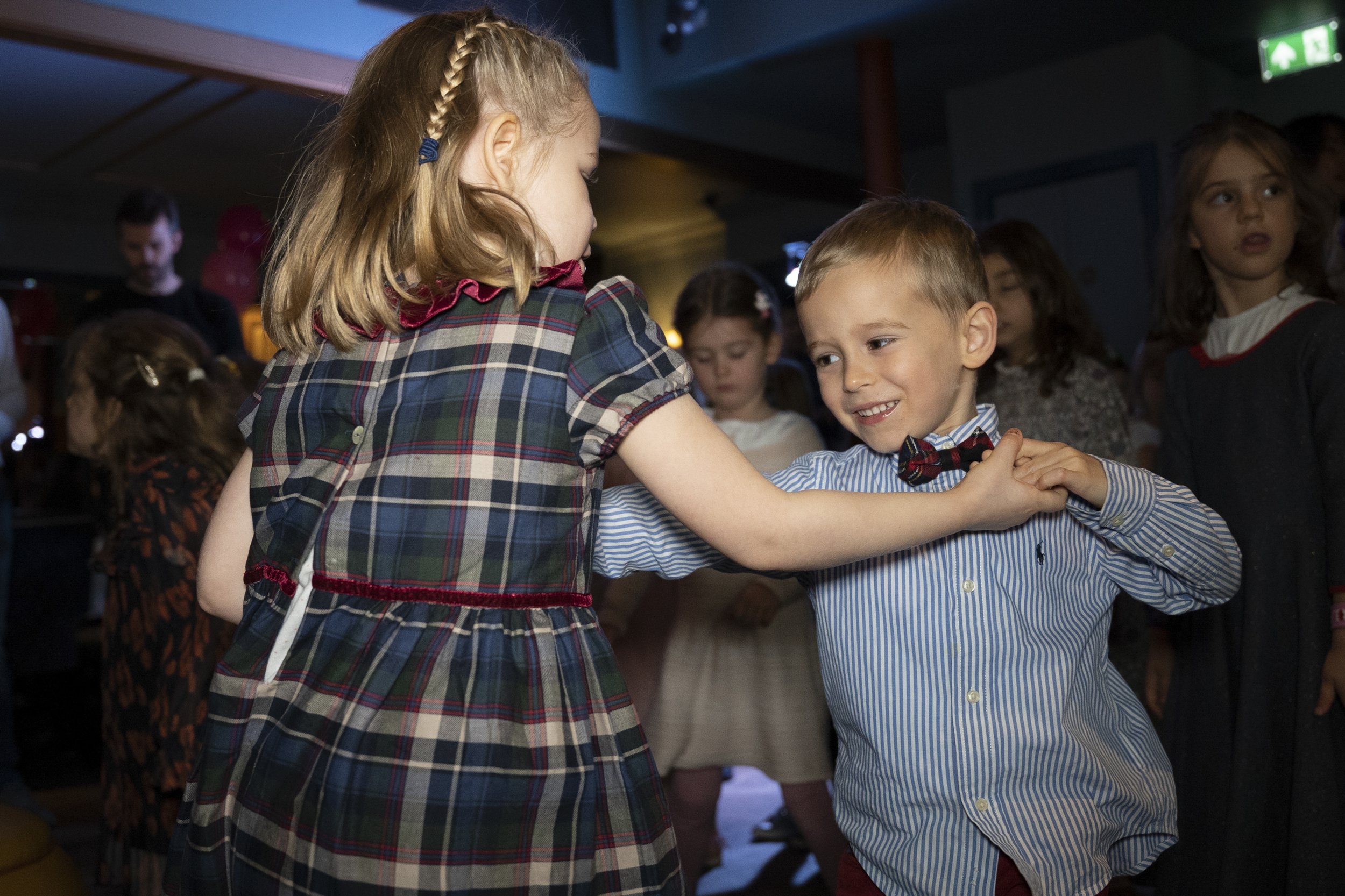 Two children dancing together at a party, surrounded by other kids in a dimly lit room.
