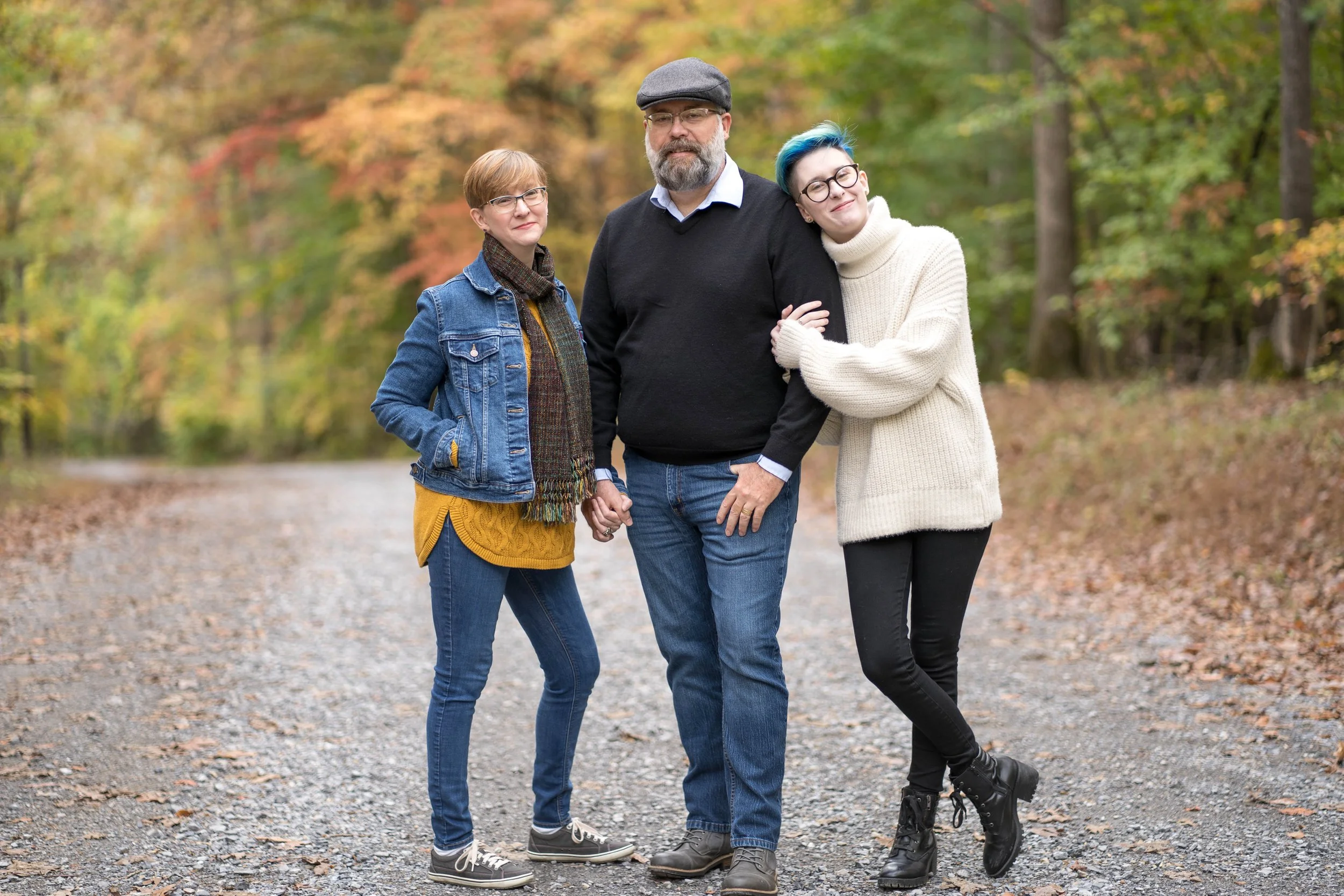A mother, father, and daughter standing in the woods on a fall day.