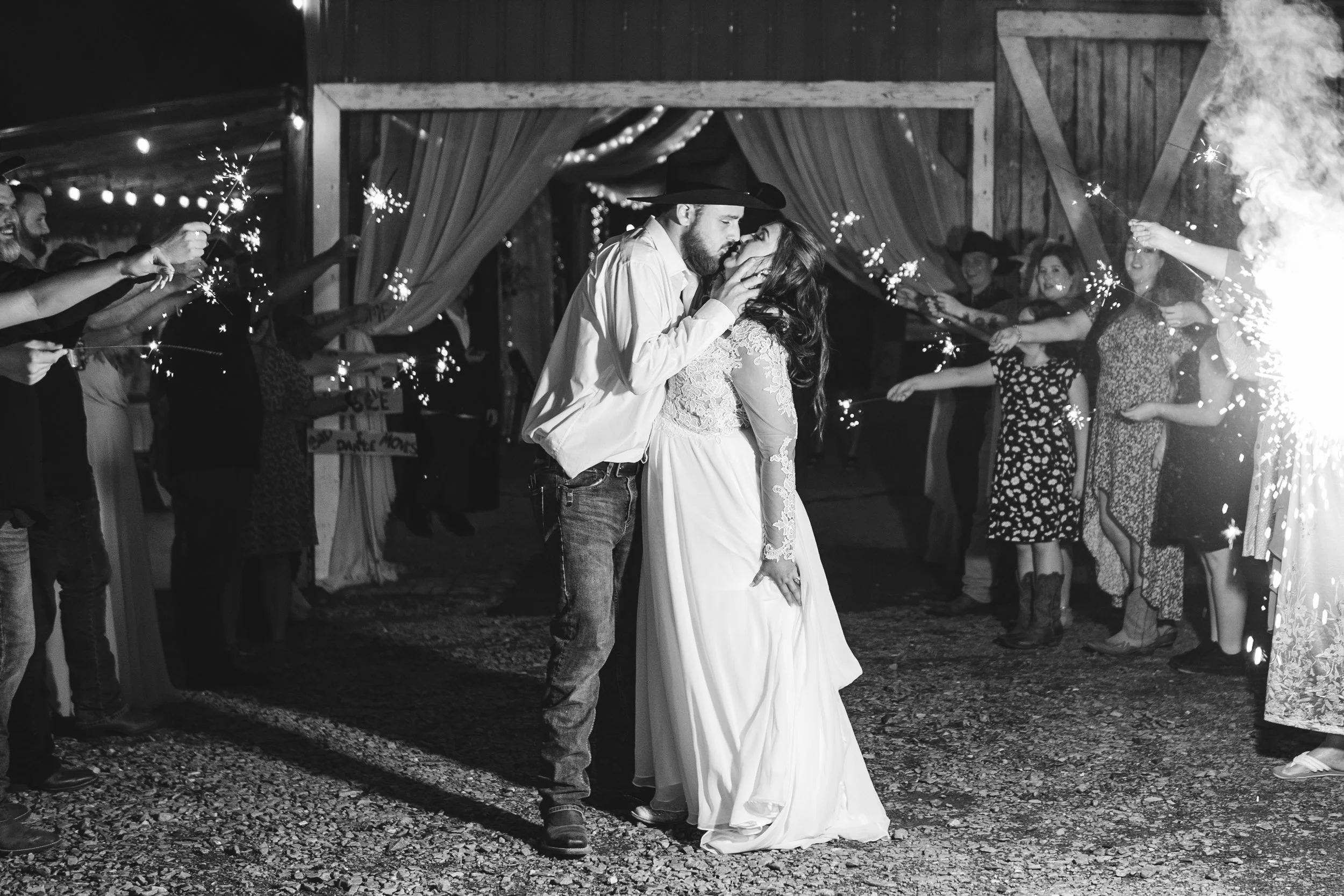 Black and white photo of a newlywed couple dancing at their outdoor wedding reception, surrounded by friends holding sparklers.