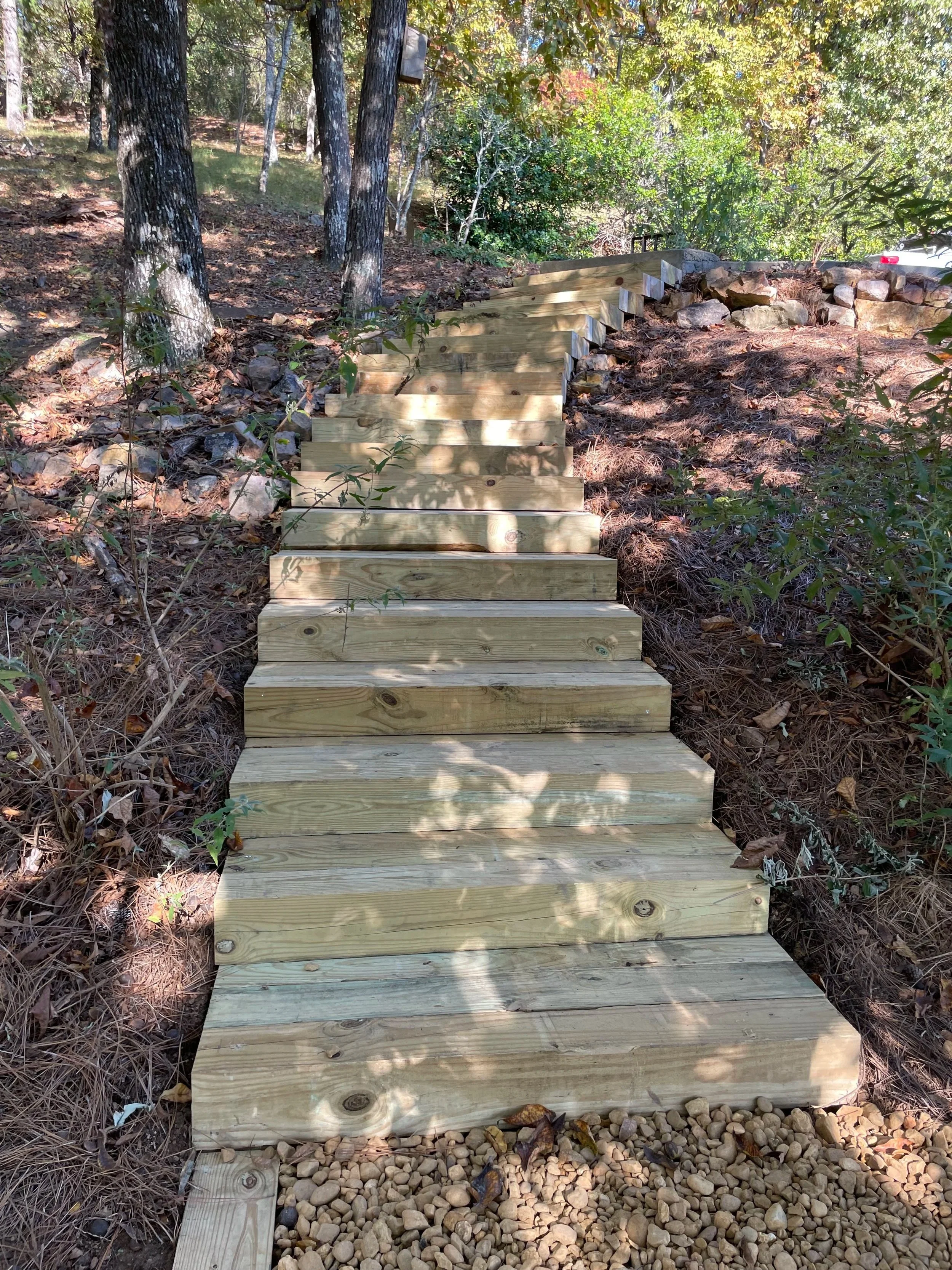 Wooden stairs leading uphill through a wooded area with trees and shrubs.