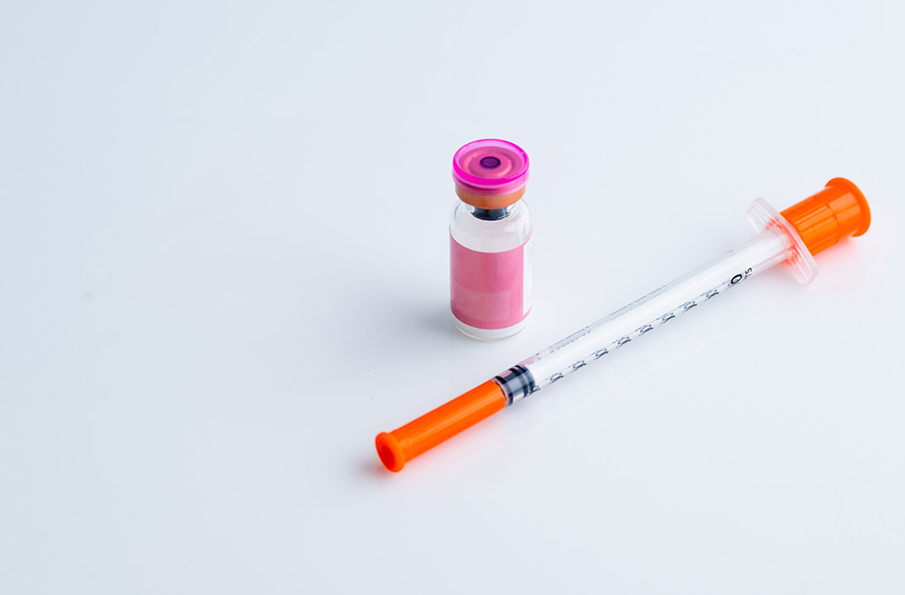 A medical syringe and a small vial of vaccine or medication on a white background.