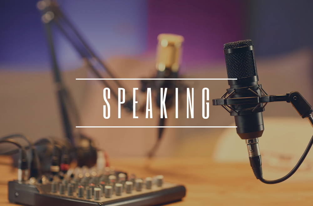 A microphone on a stand and a mixer on a wooden table in a recording studio with the word 'Speaking' overlaid.