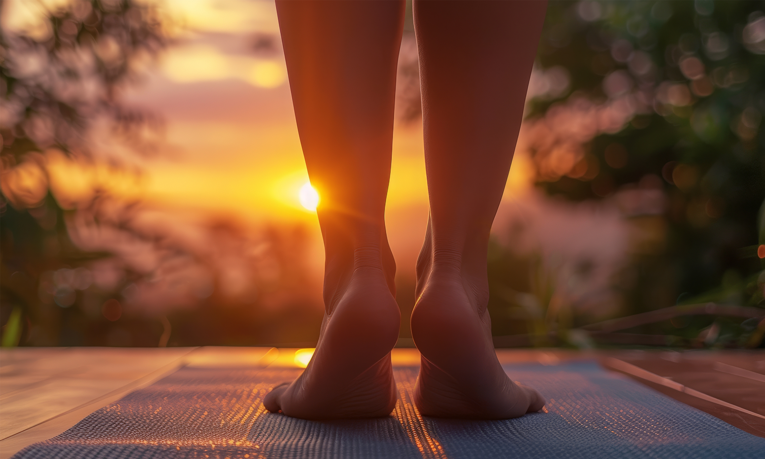 Person practicing yoga outdoors during sunset, focusing on their feet and legs on a yoga mat.