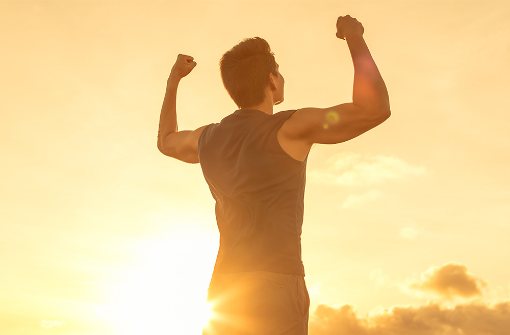 A man flexing his muscles outdoors at sunset, showing strength and confidence.