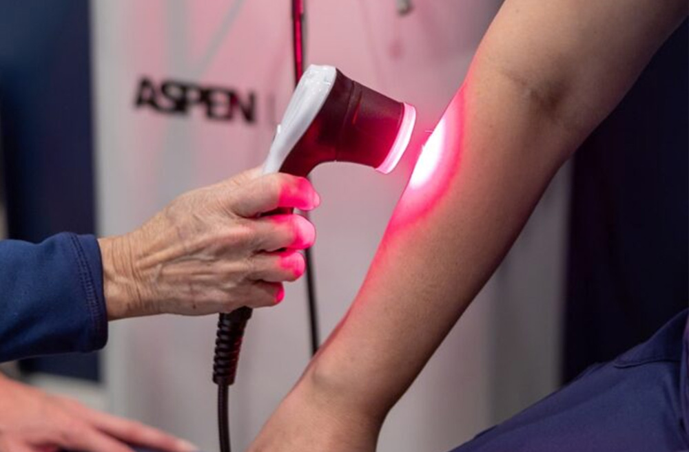 Person using a laser device on a person's forearm during a skin treatment, with a red glow from the laser.