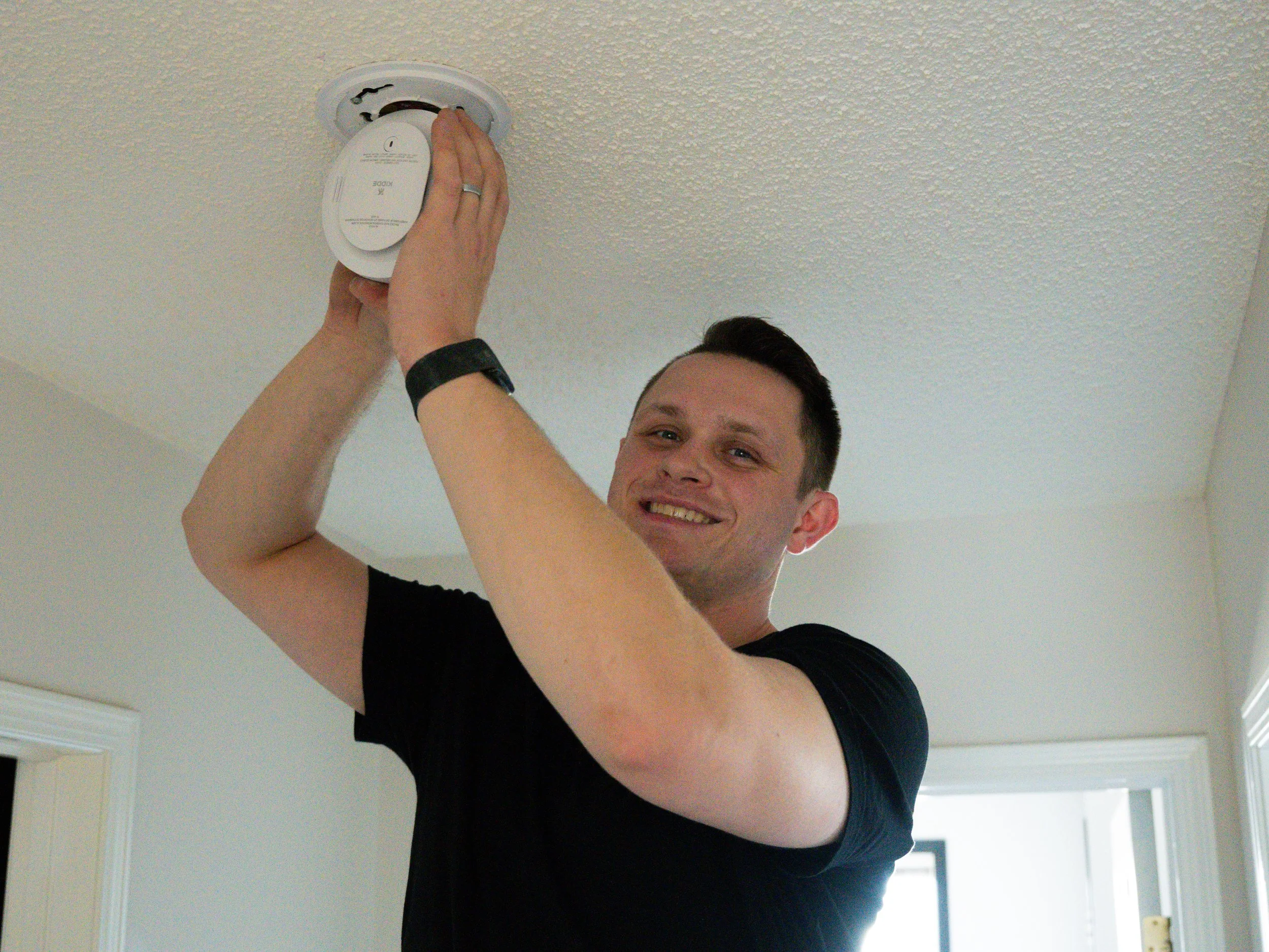 A man installing a smoke detector on the ceiling of a room.