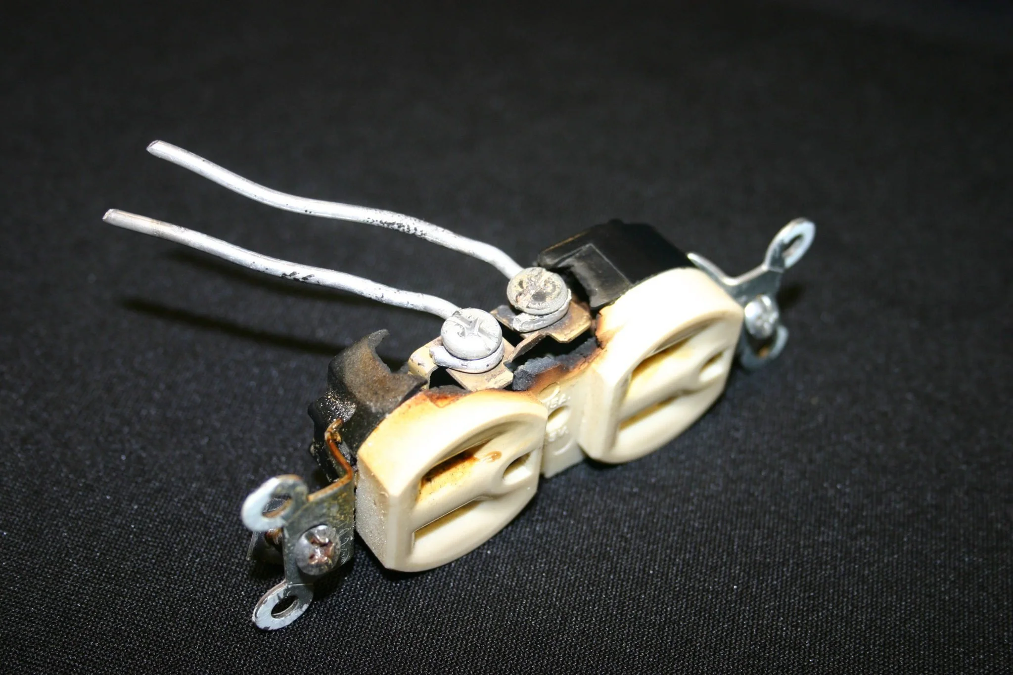Close-up of a vintage electrical switch with two ivory-colored toggle levers, attached to metal screws and wires, on a black surface.