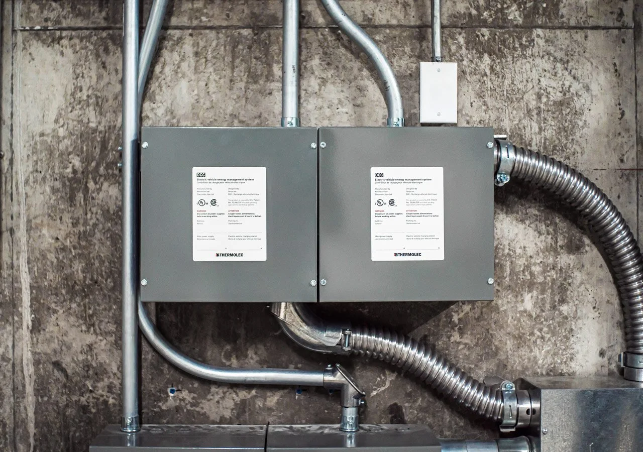 Electrical vehicle energy management system boxes mounted on a concrete wall with metal conduits connected.