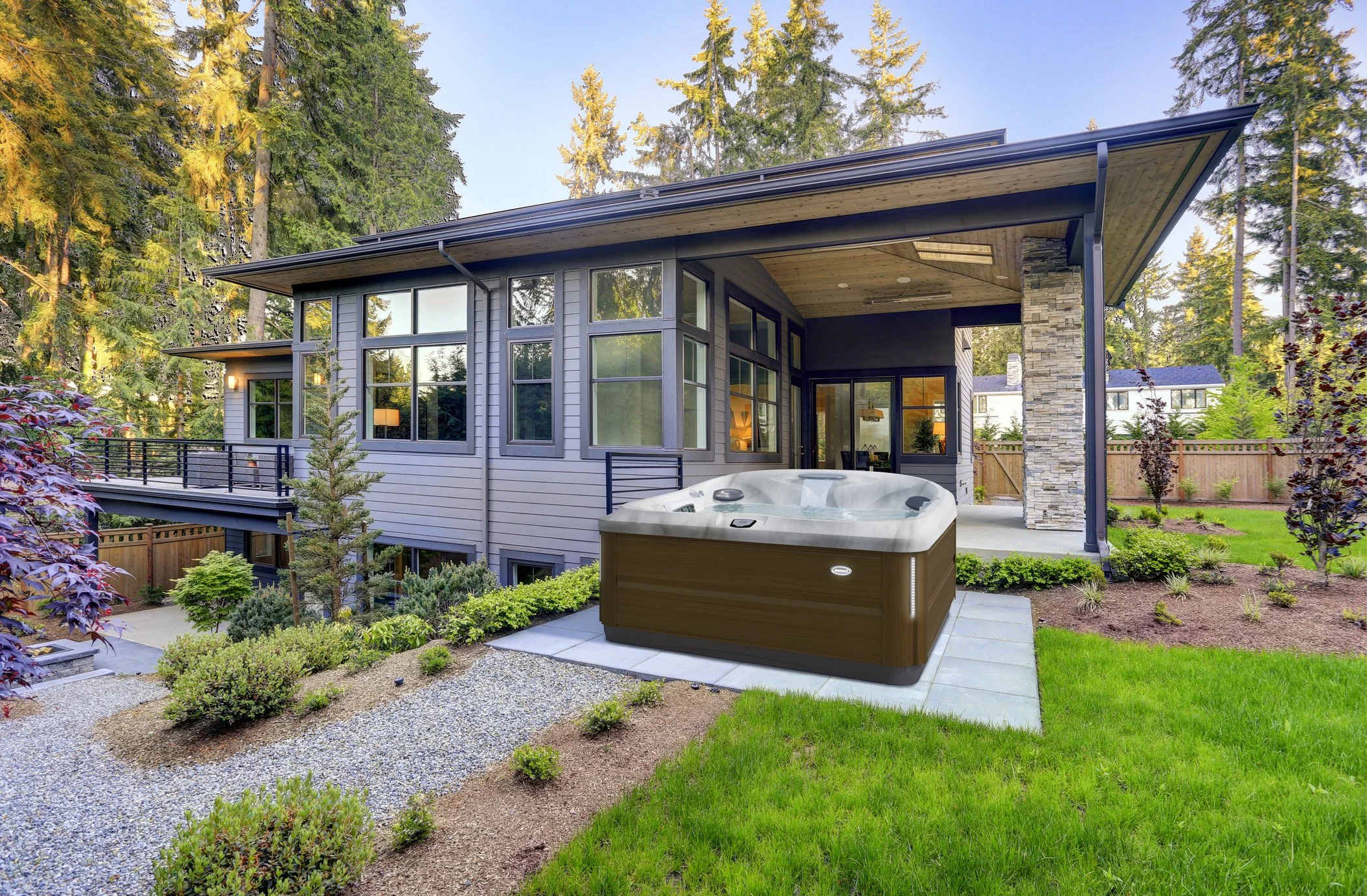 Modern house with large windows, surrounded by trees and landscaping, with a hot tub on a patio in the backyard.