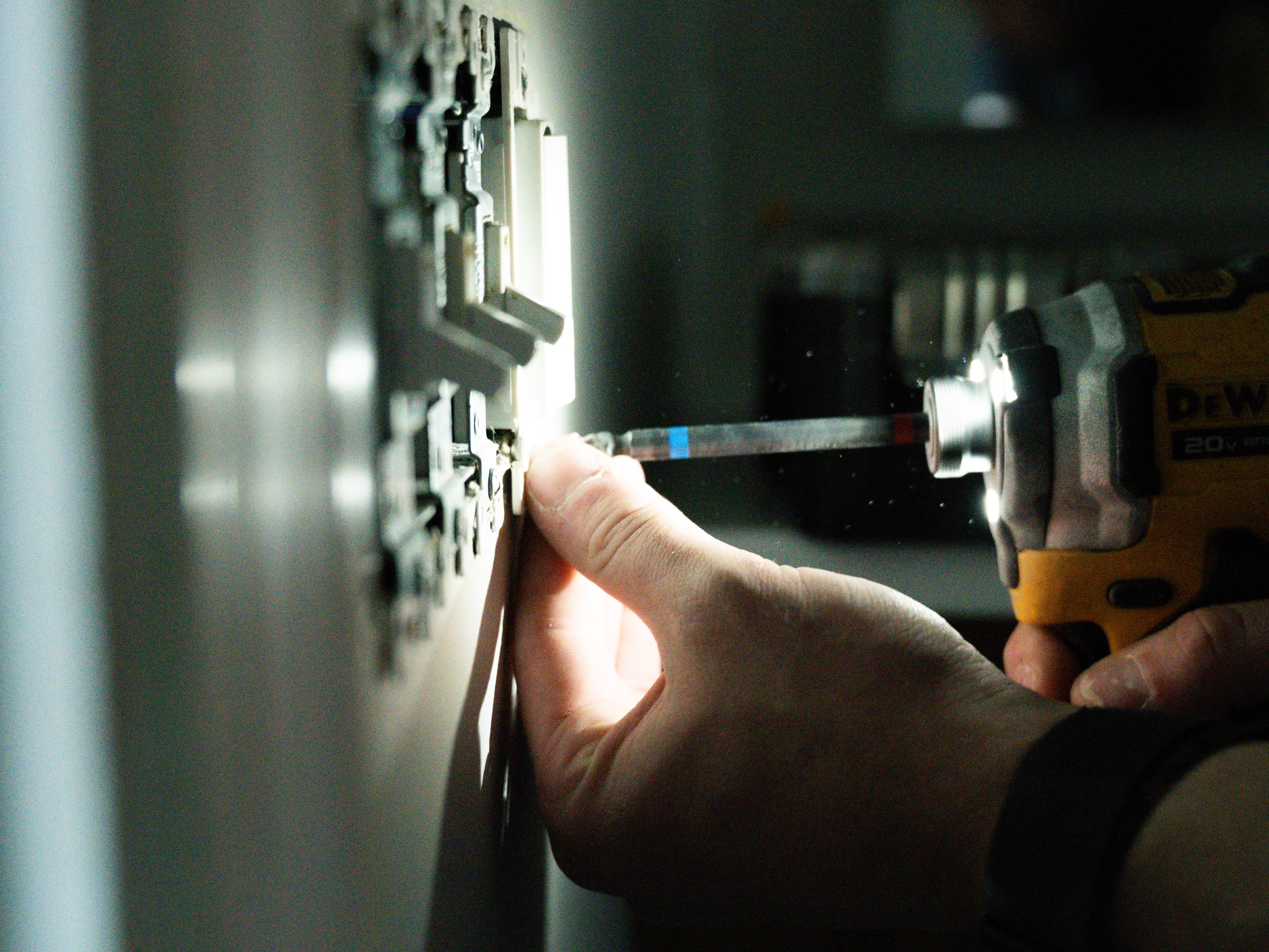 A person using a power drill to work on an electrical panel or circuit breaker box.