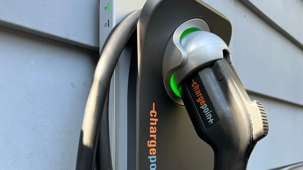 An electric vehicle charging station with a charging plug inserted and green indicator lights.