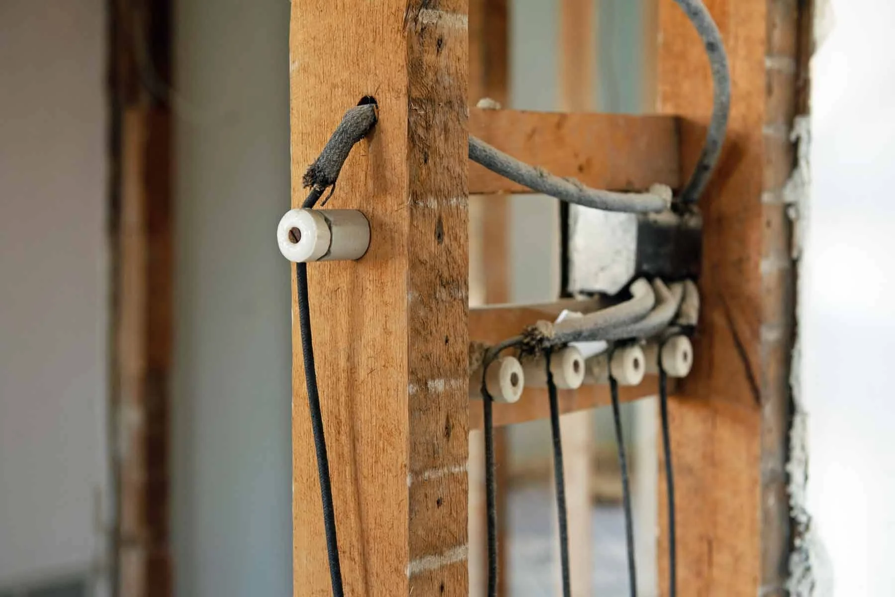 Close-up of electrical wiring and ceramic insulators attached to a wooden frame during construction.