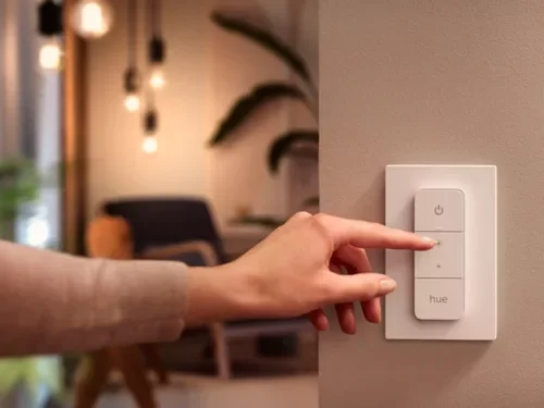 Person pressing a button on a wall switch with a smart lighting control panel labeled 'hue' in a modern interior.