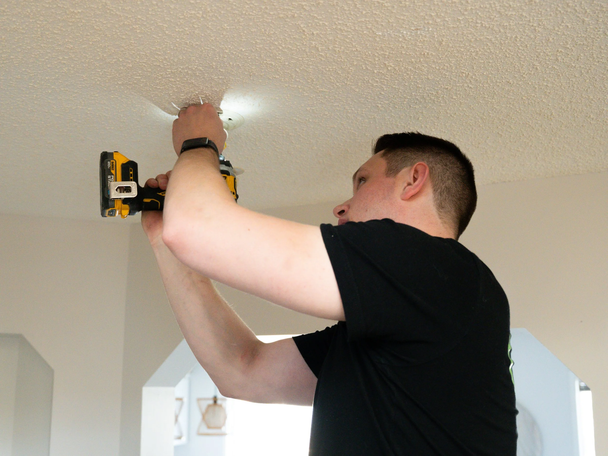 Man installing or fixing smoke detector on ceiling using a drill.