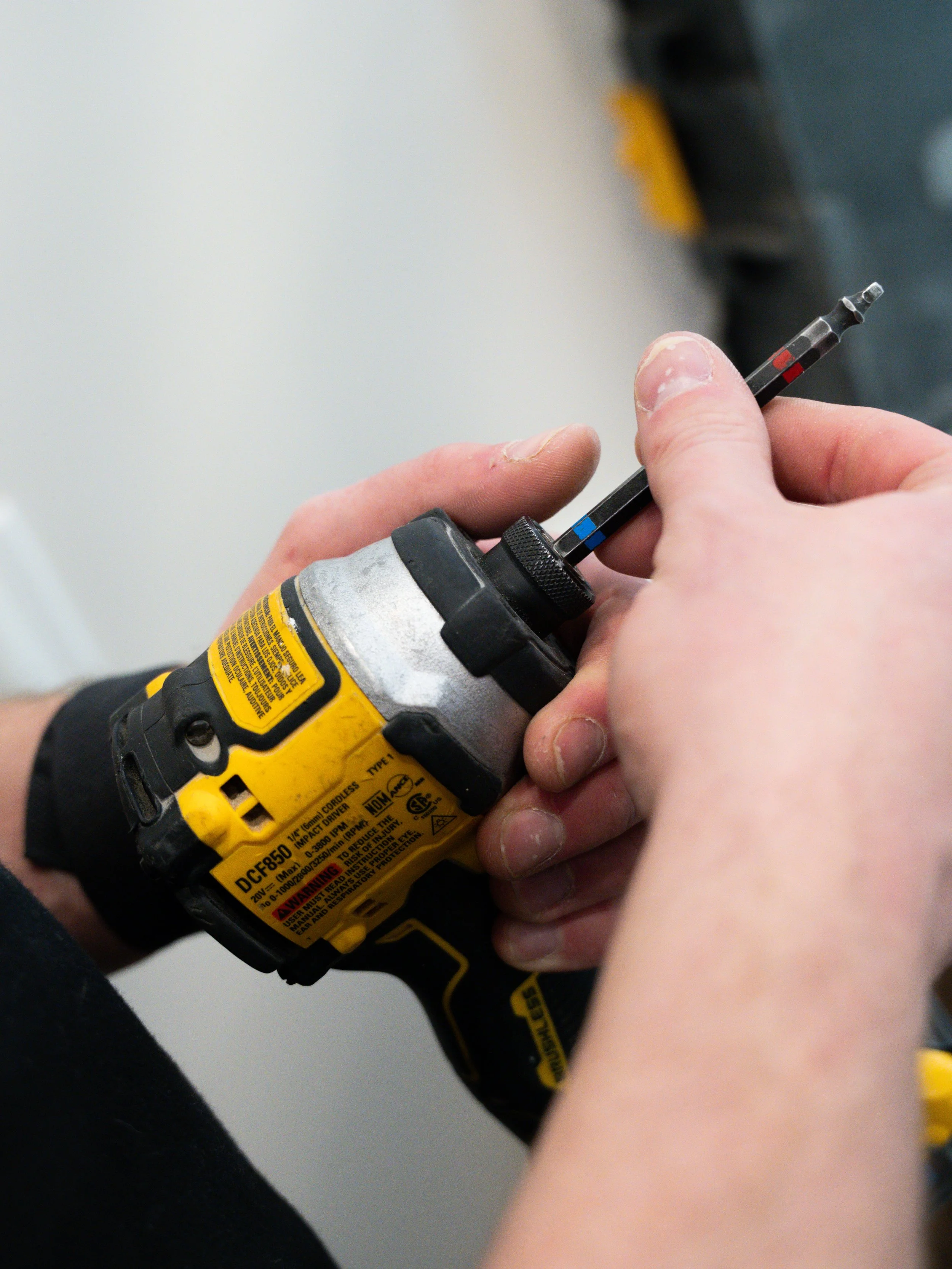 A person holding a yellow cordless power drill with one hand and inserting a screwdriver bit into the drill's chuck with the other hand.