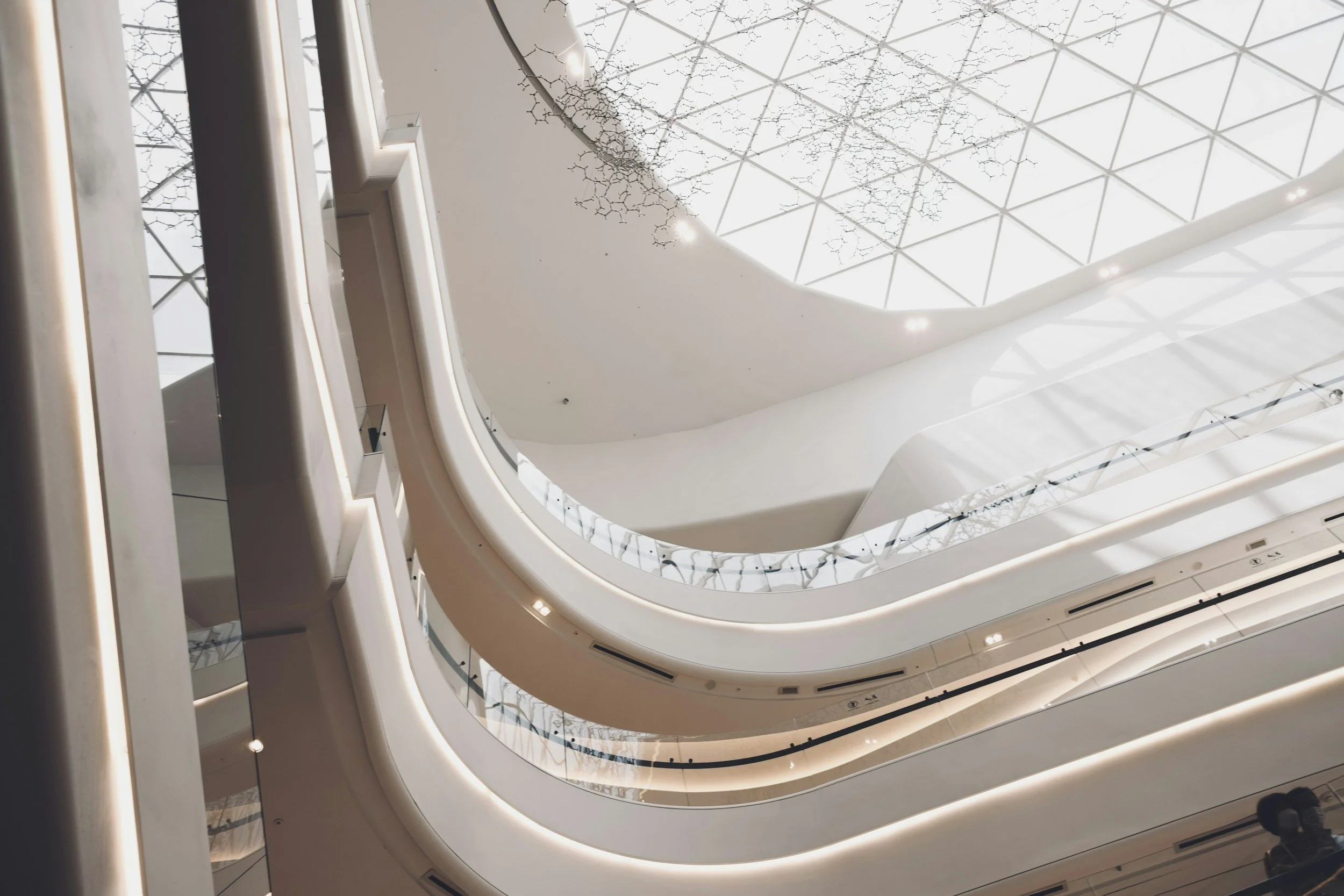 Inside view of a modern multi-level shopping mall with white curved balconies and a glass ceiling.