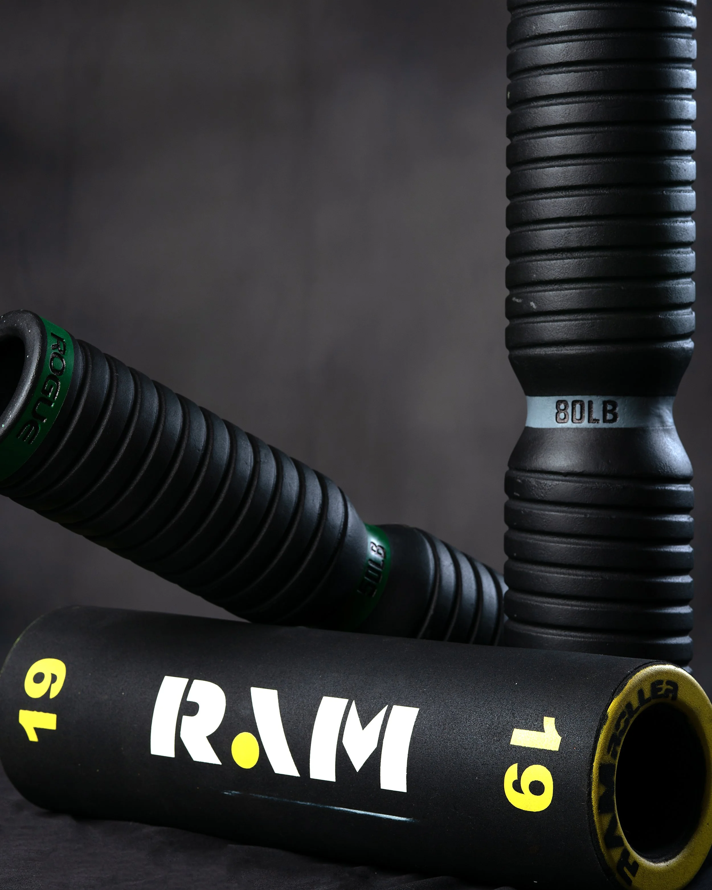 Black tempering roller, including a 80 pound and a 19 pound roller, with textured handles and yellow and green markings, arranged on a dark surface.