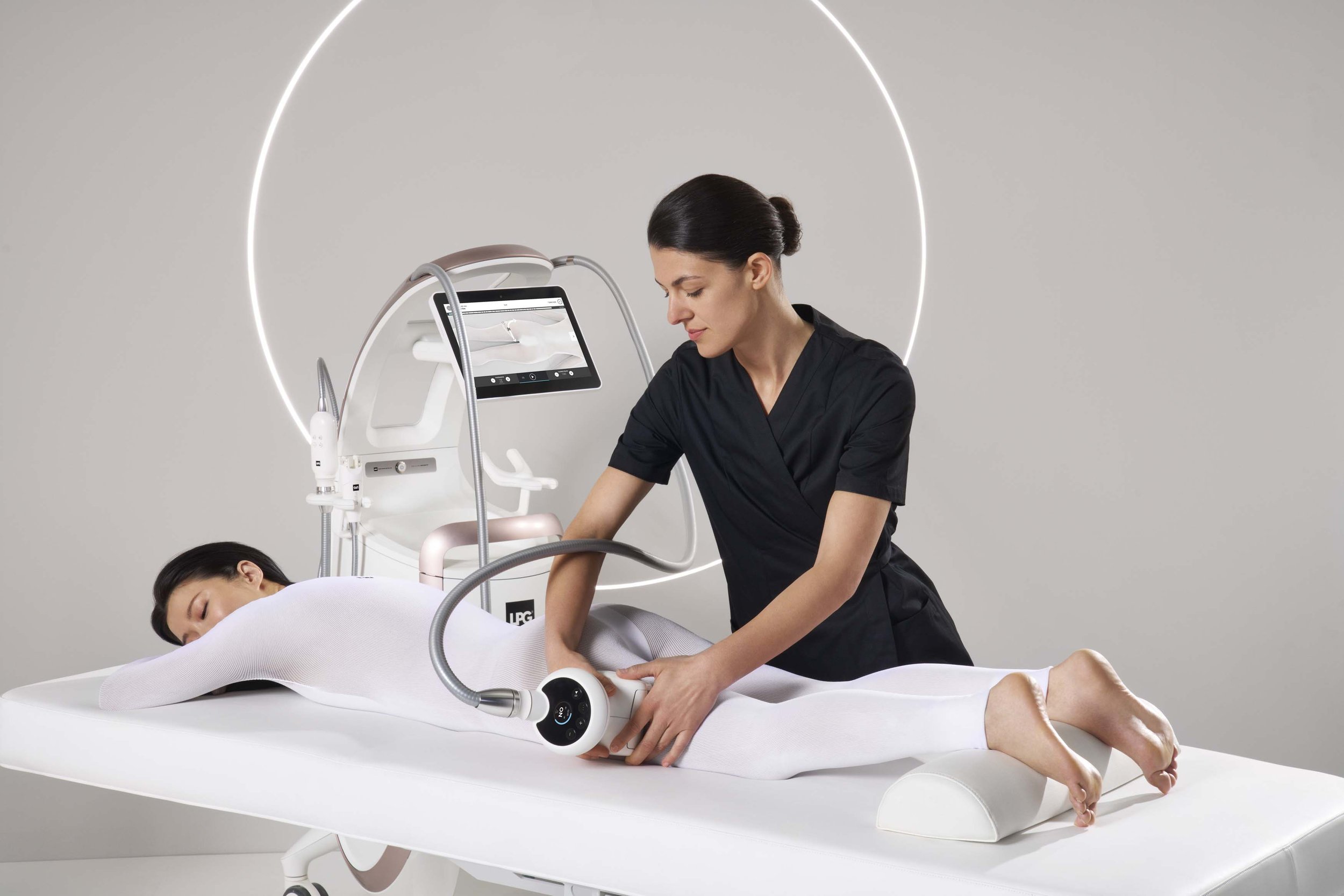 A woman lying face down on a medical bed receiving a treatment with medical equipment and a technician attending to her.
