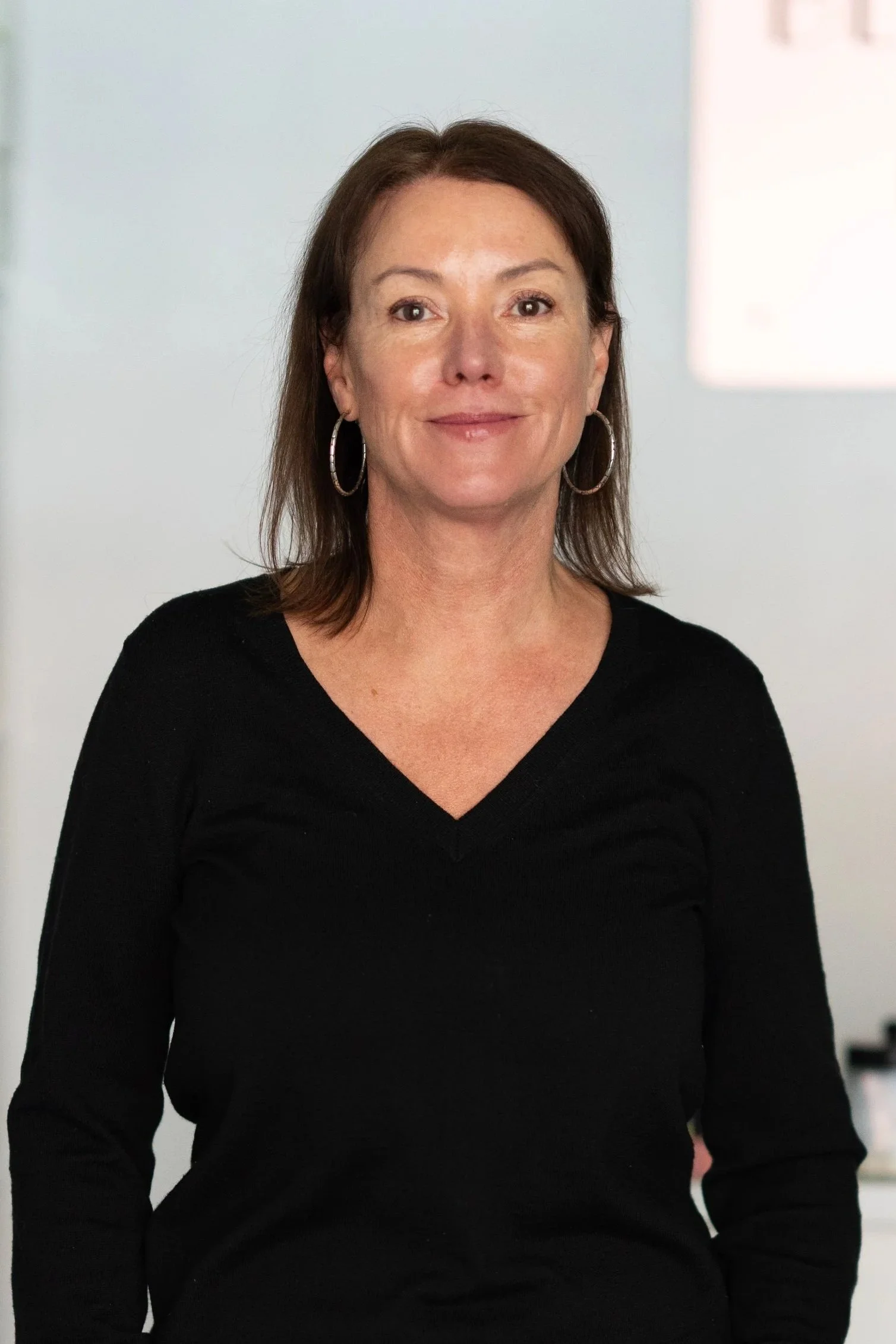 A woman with shoulder-length dark brown hair smiling, wearing a black outfit