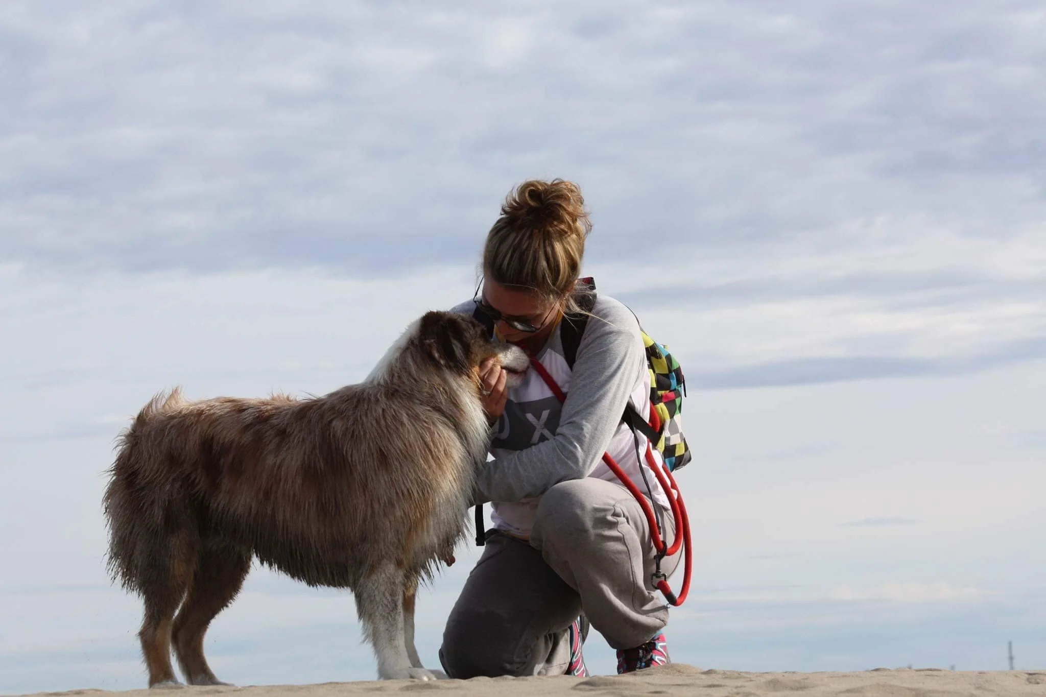 Une femme agenouillée face à un chien de berger australien sur une plage, caressant doucement son visage.