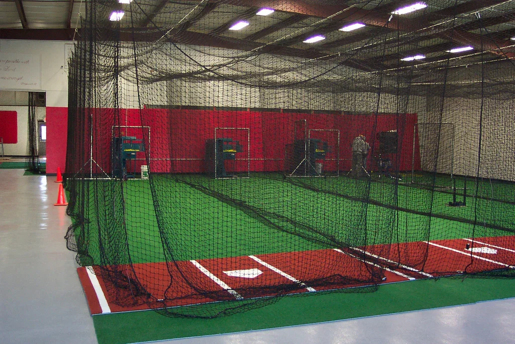 Indoor golf hitting bays with nets, artificial turf, and golf balls.