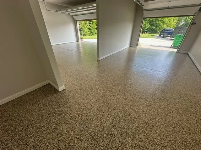 Empty garage with beige carpet, open garage doors, and a view of green trees outside.