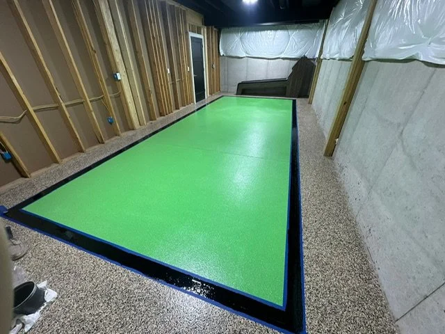 Indoor room with a partially constructed wall, insulation, a foam hockey or shuffleboard table, and some furniture in the background.
