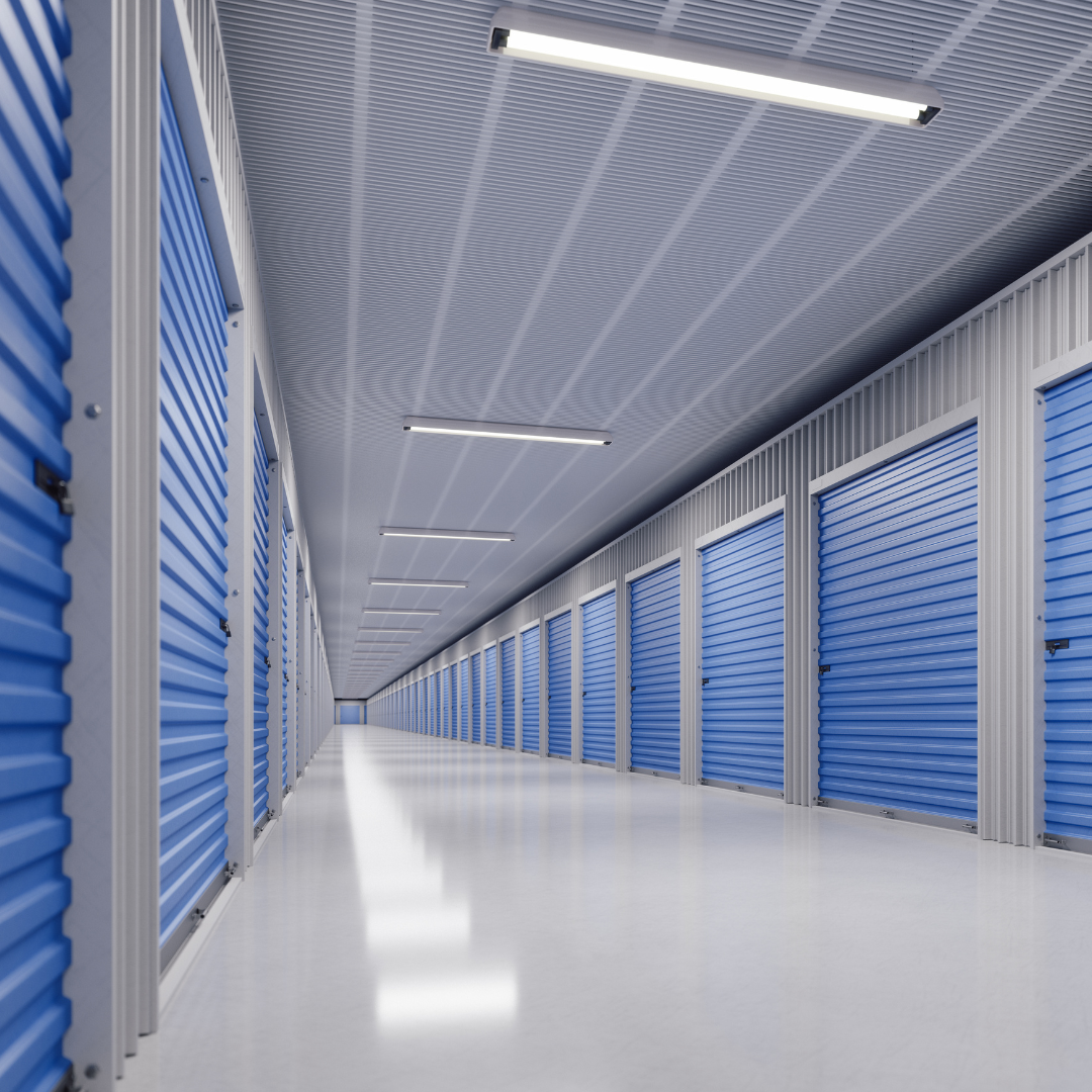 Empty storage units with blue roll-up doors in a corridor within an indoor storage facility.