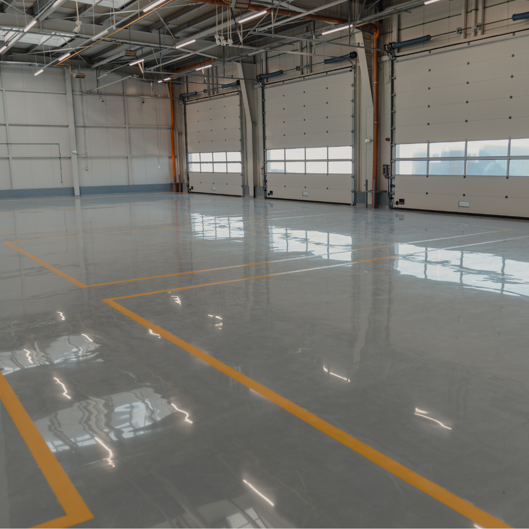 Empty indoor parking garage with polished concrete floor, yellow parking lines, and large garage doors with windows.