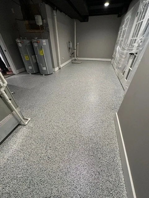 Empty utility or laundry room with water heaters, pipes, and a soap or cleaning spray on the floor.